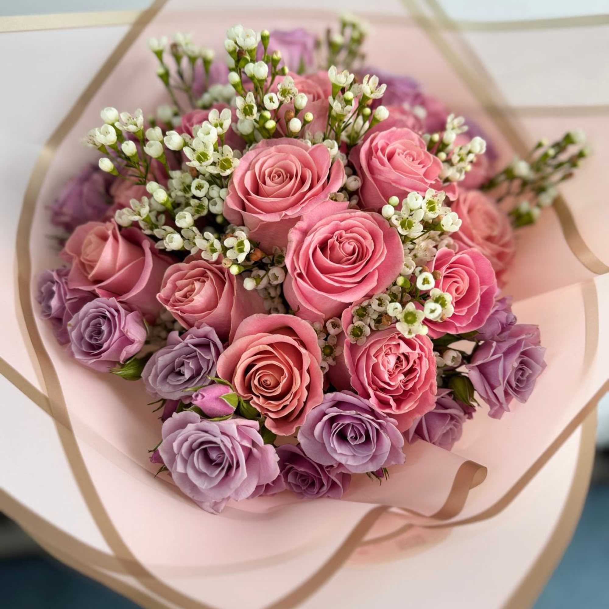 Bouquet of pink and lavender roses wrapped in pale pink paper