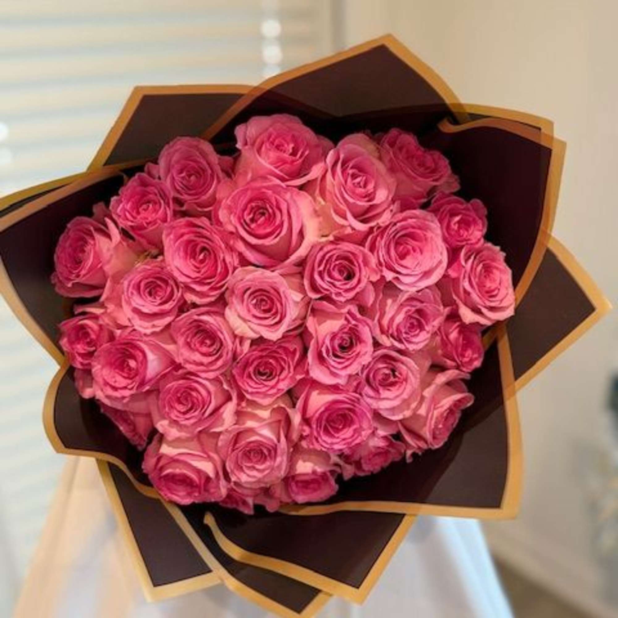Bouquet of pink roses wrapped in dark paper with gold trim