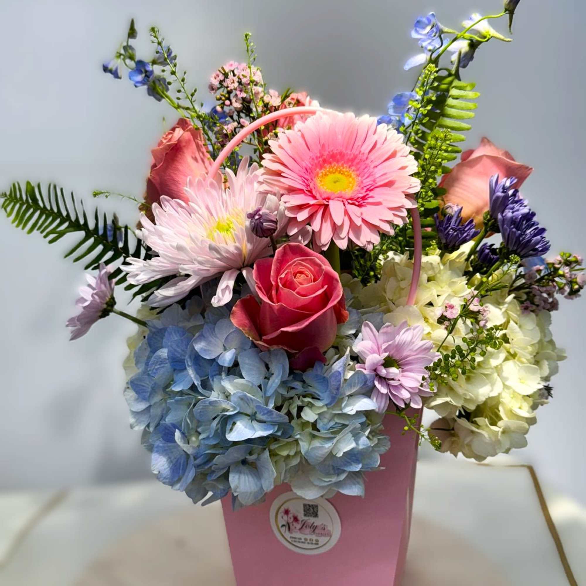 Pink and blue mixed flower arrangement in a pink box with a handle