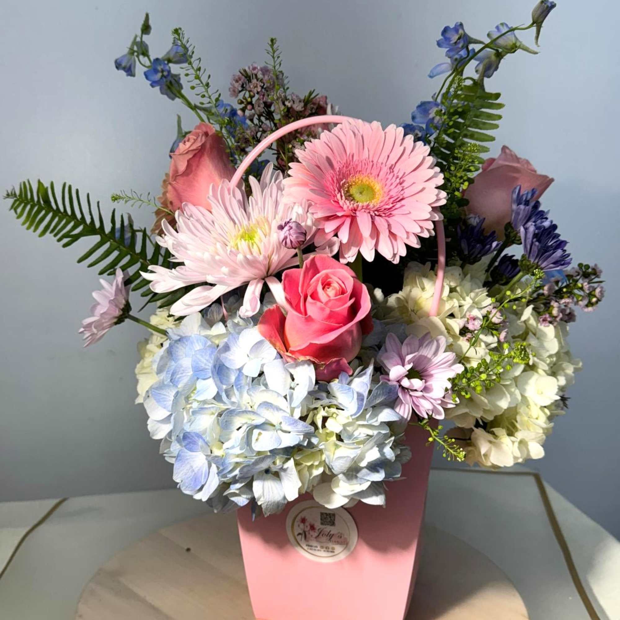 Pink and blue mixed flower arrangement in a pink box with a handle