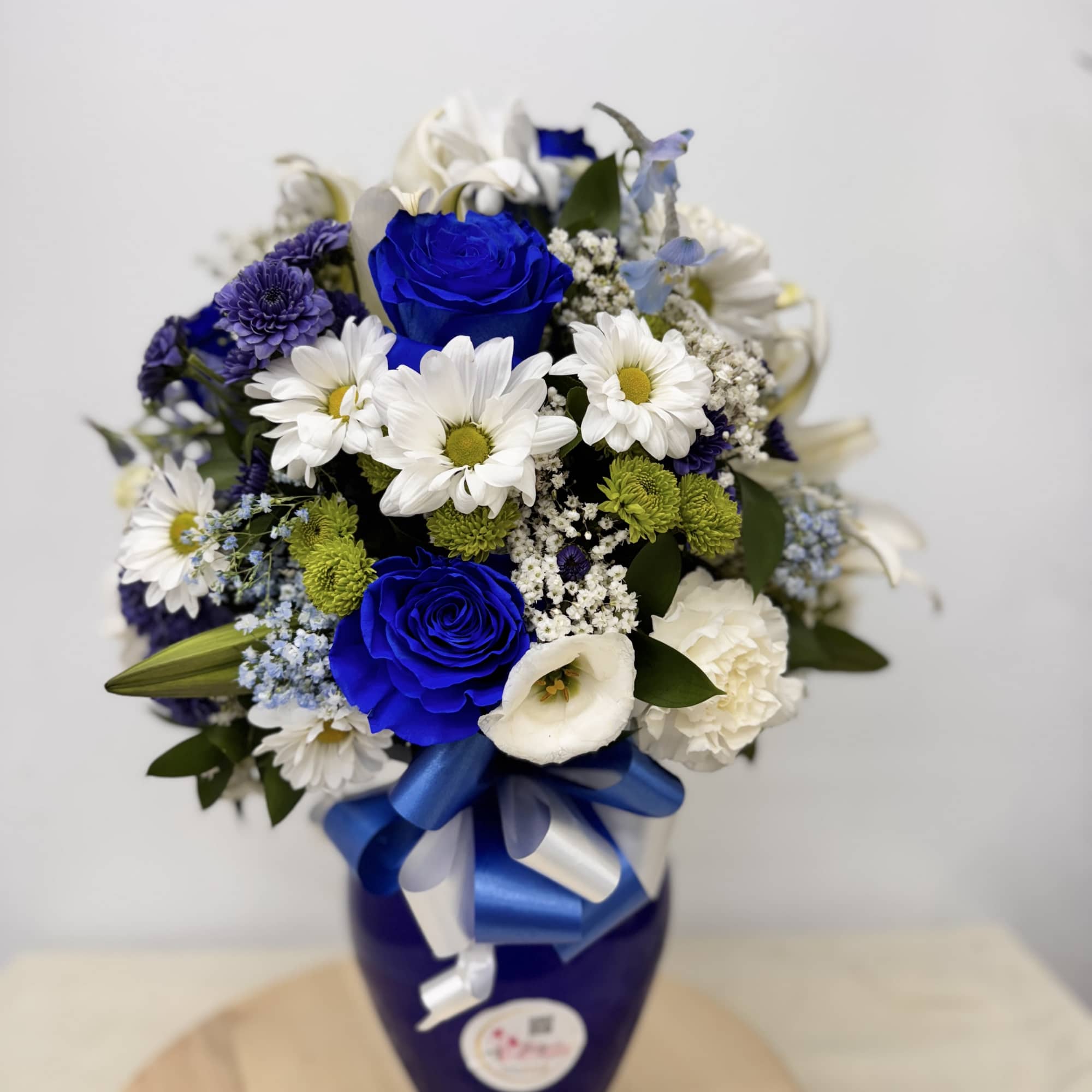 Blue and white flower bouquet in a dark vase with a ribbon