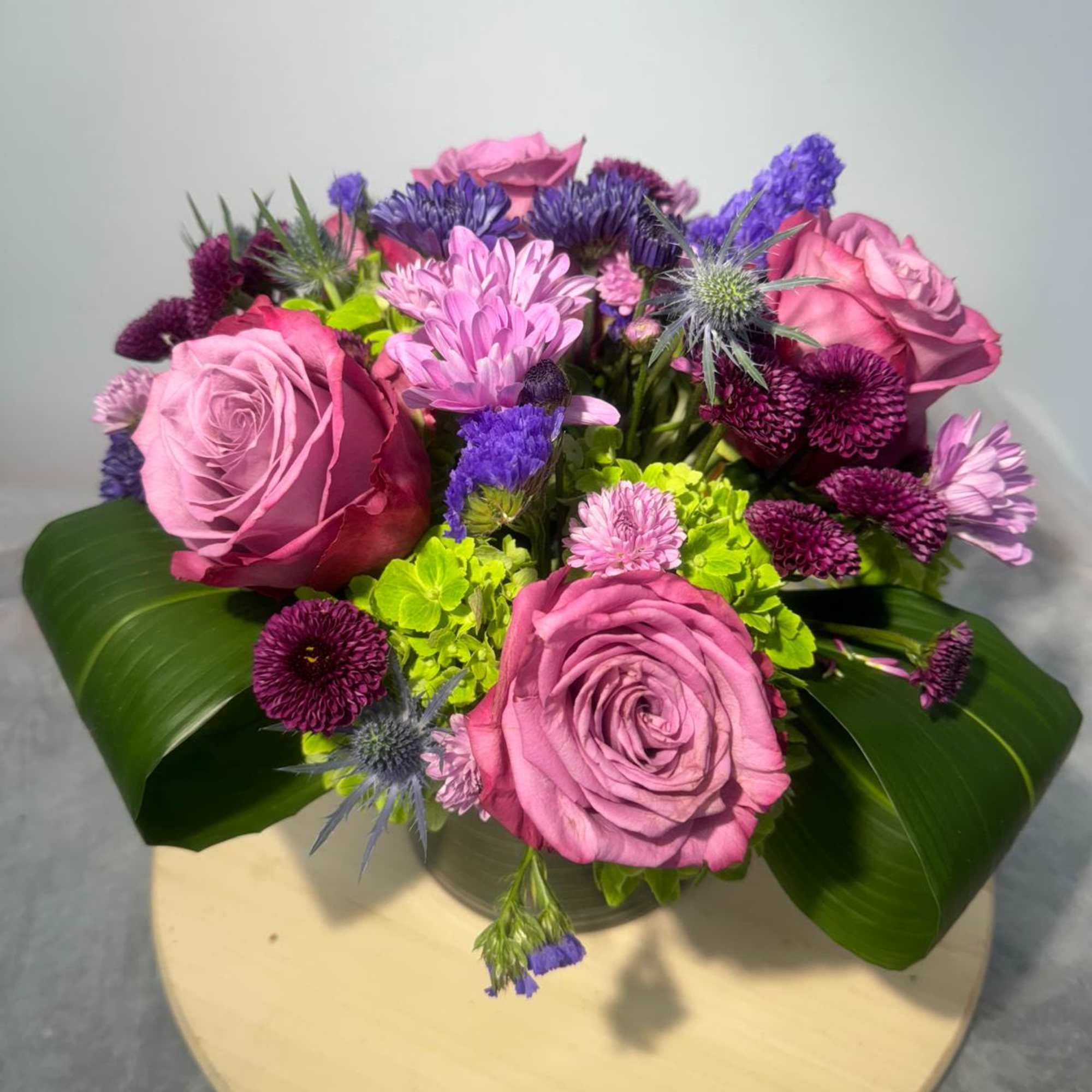 Pink roses and purple mixed flowers arranged in a low bouquet.
