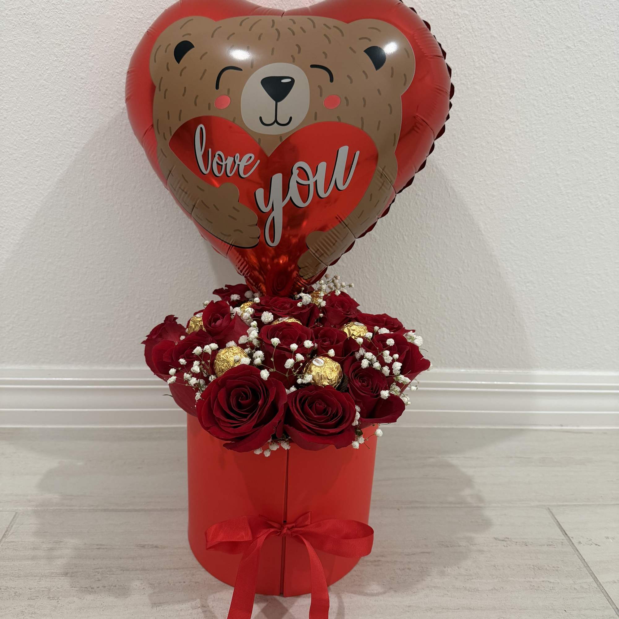 Red rose arrangement in a red box with a heart-shaped teddy bear balloon