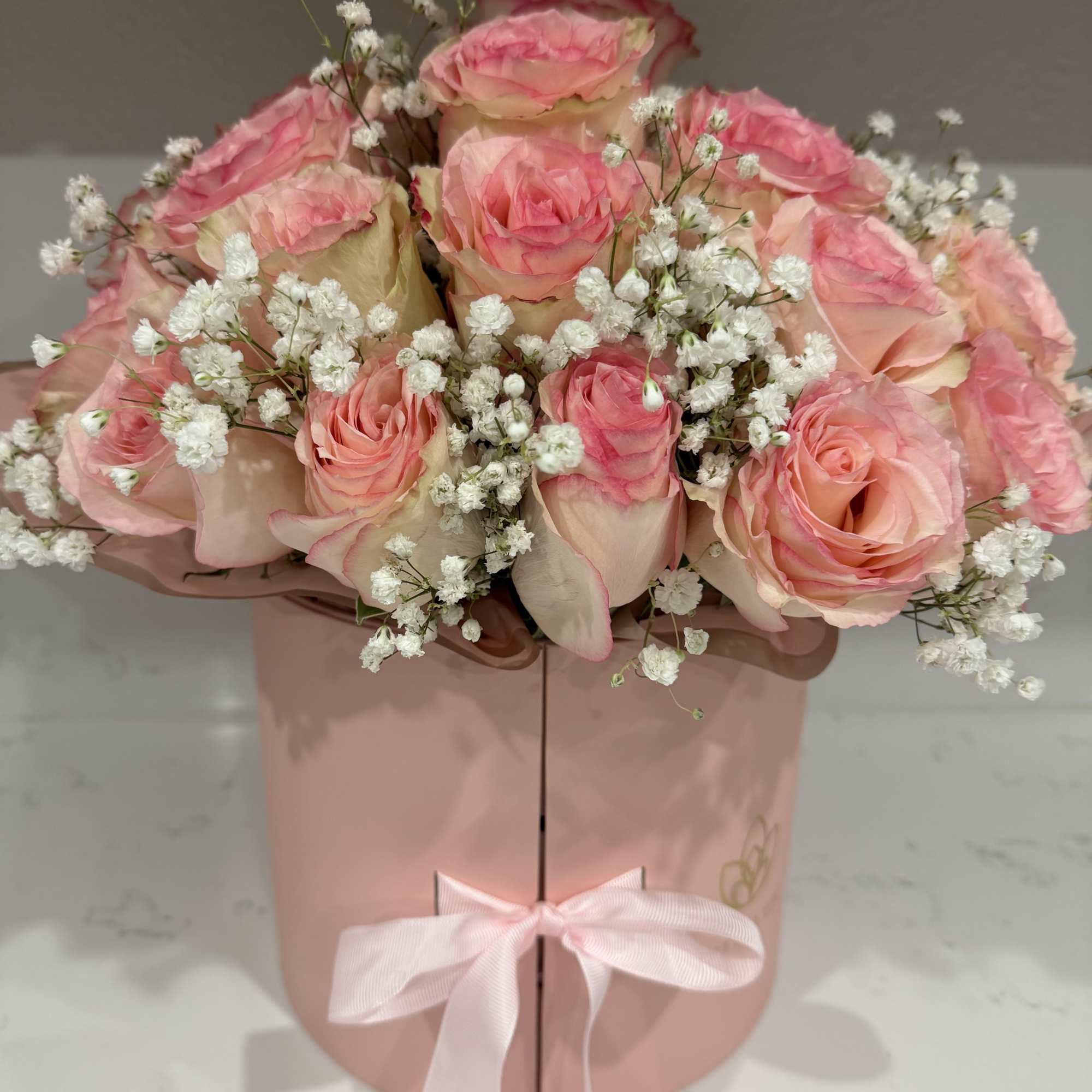 Pink roses with white baby's breath in a pink gift box tied with a ribbon