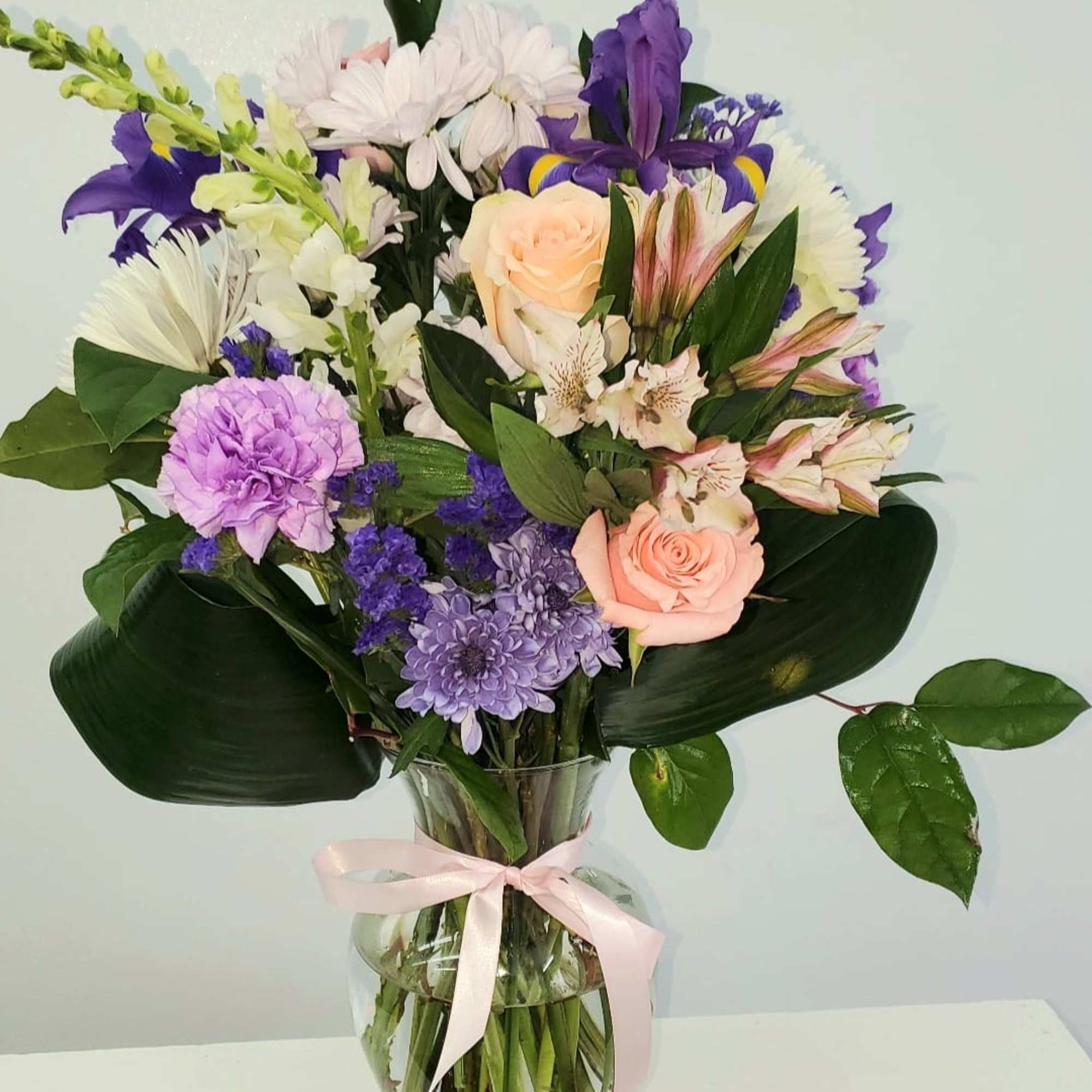 Mixed bouquet of pastel flowers in a clear glass vase with a pink ribbon