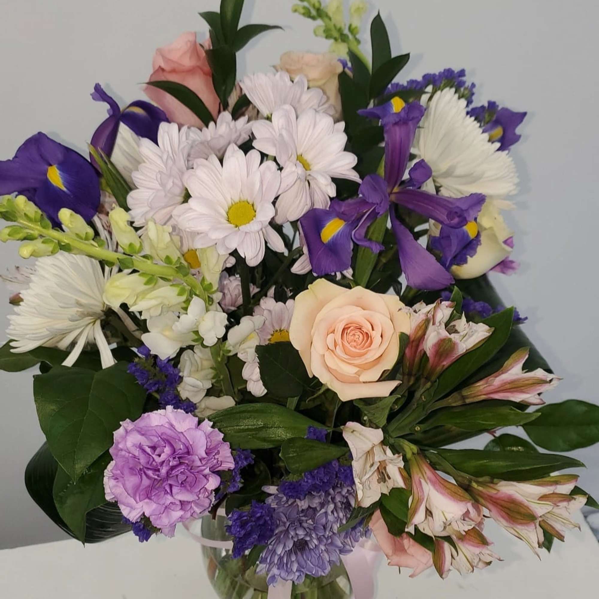 Mixed bouquet of roses, daisies, irises, and alstroemeria in a glass vase