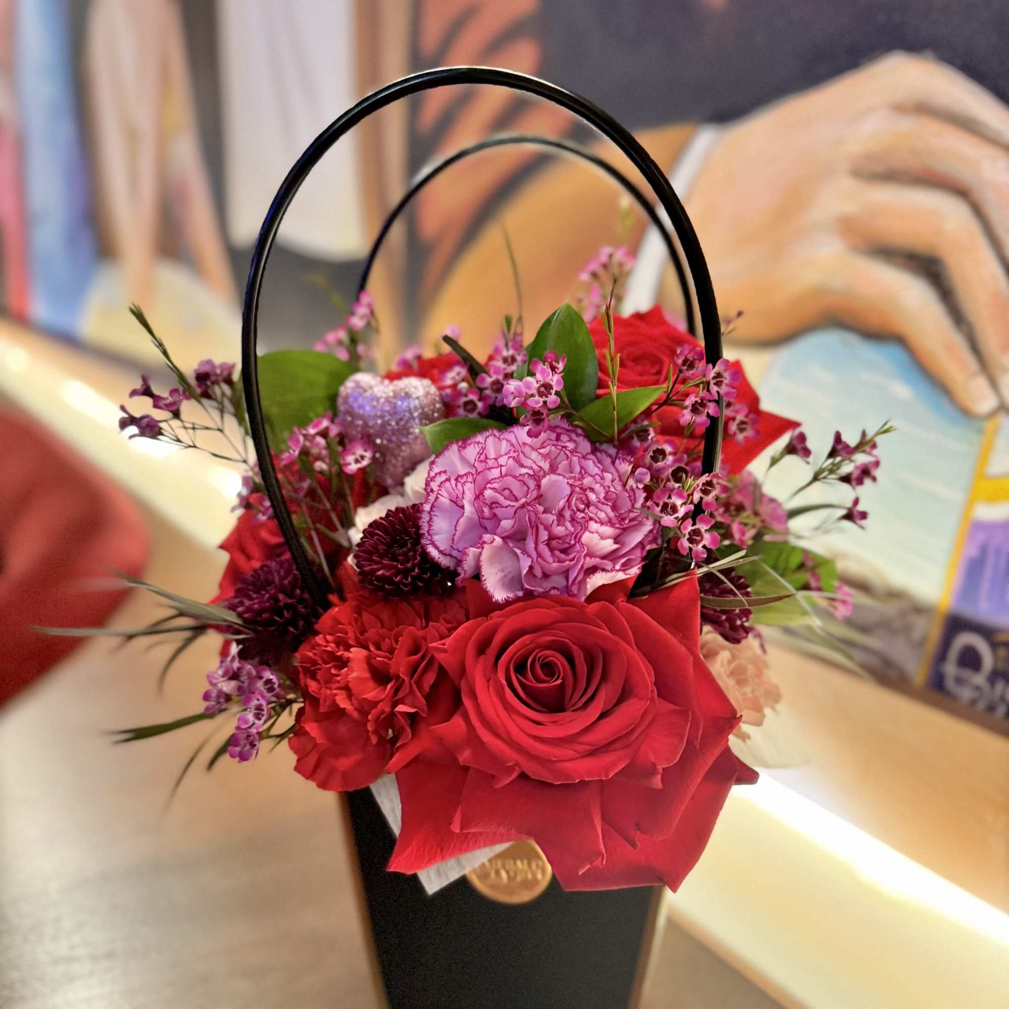 Red and pink floral arrangement in a black handled box