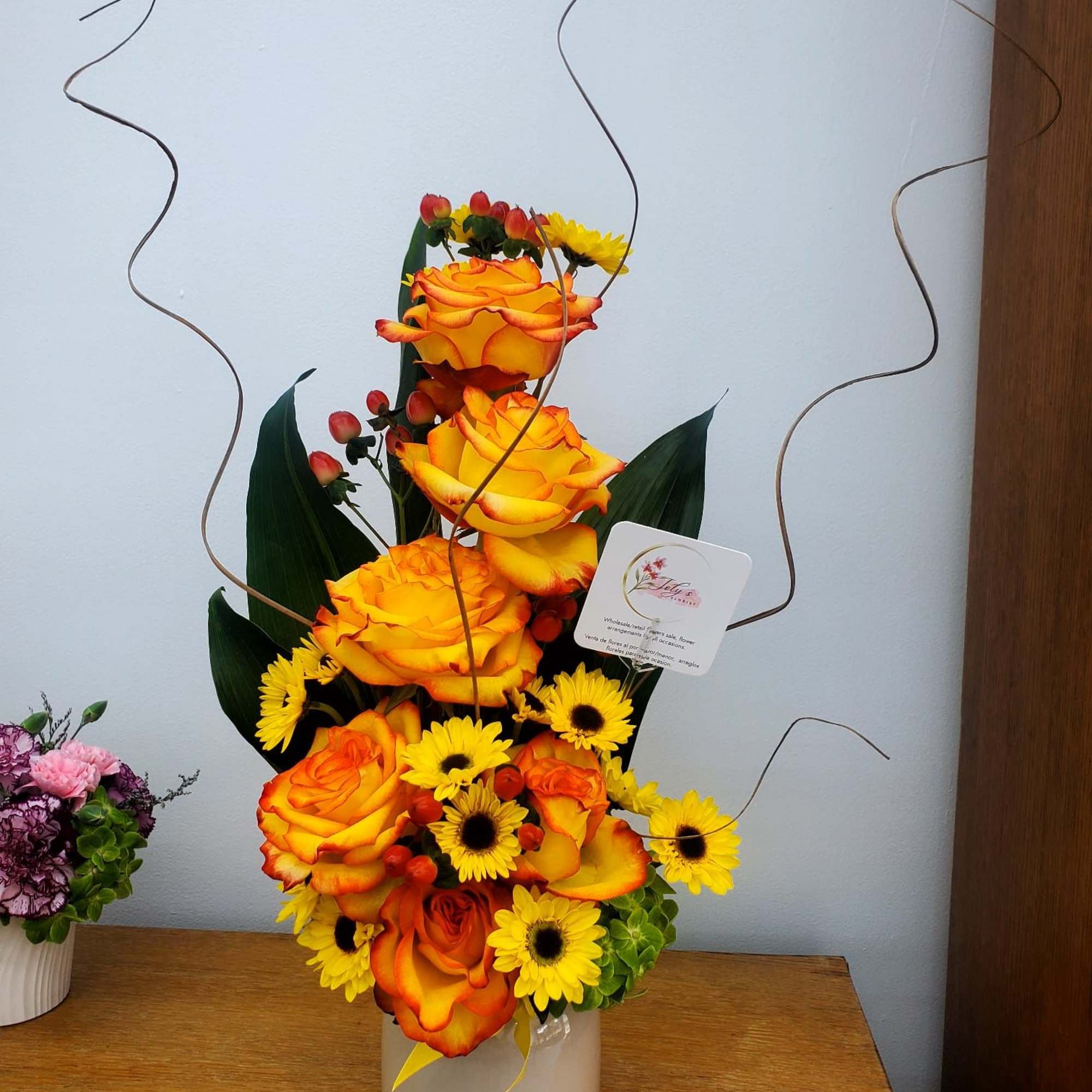 Tall arrangement of orange roses and yellow daisies in a white vase