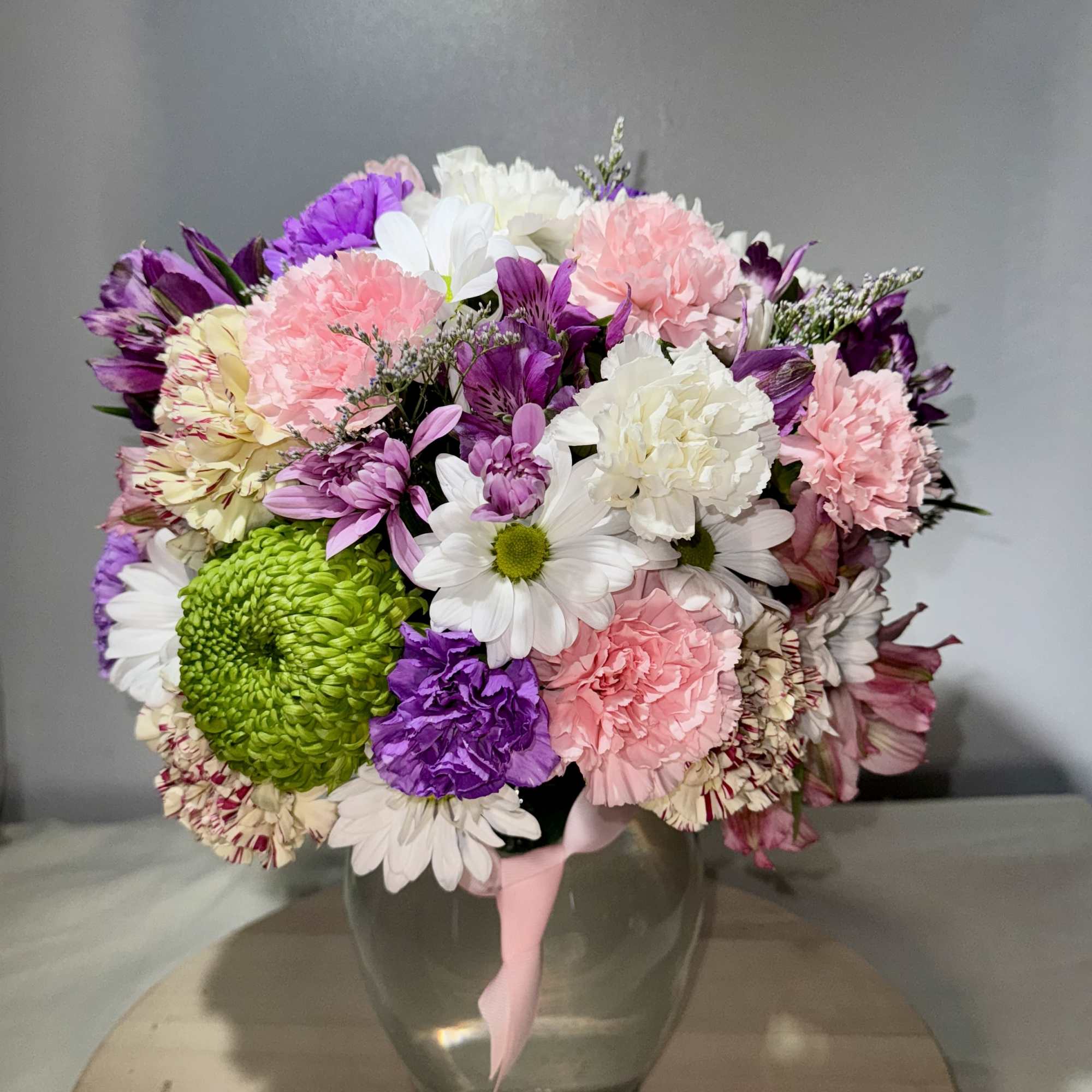 Mixed bouquet of pink, purple, white, and green flowers in a glass vase