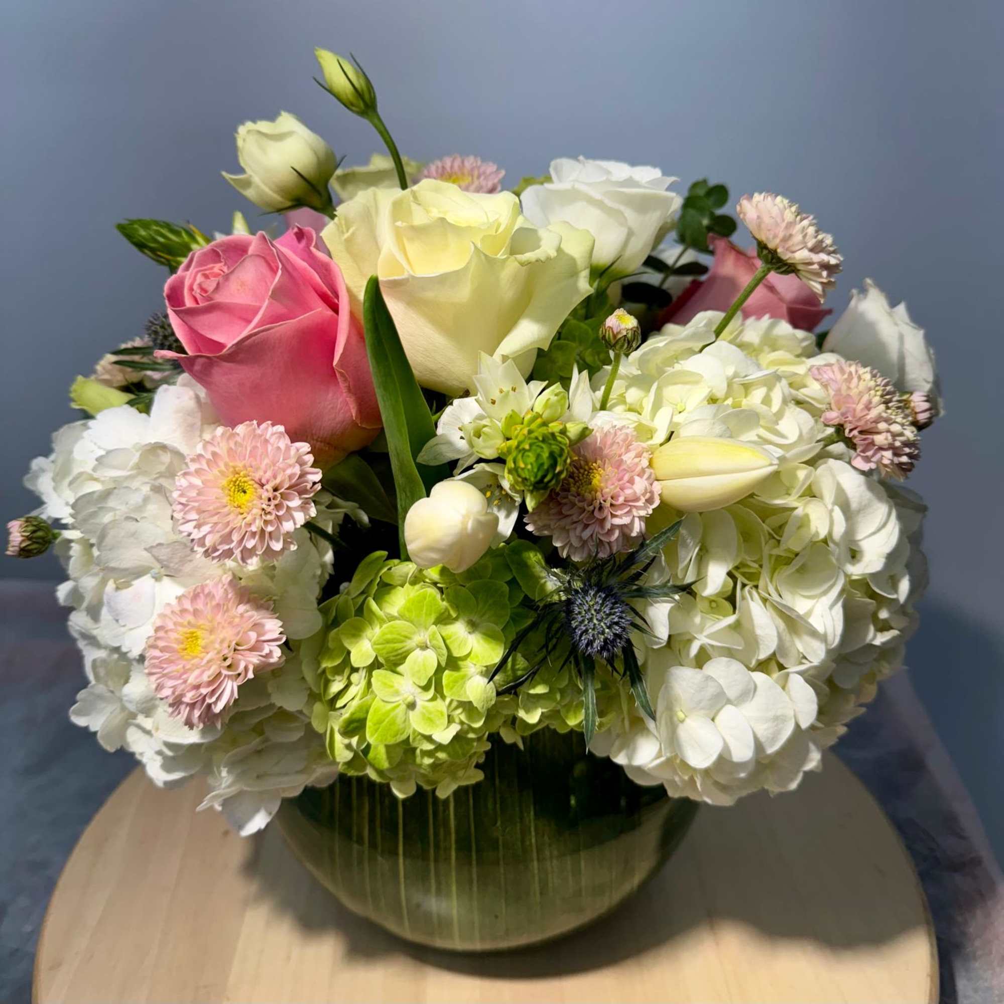 Mixed bouquet of pink and white roses, hydrangeas, and small daisies in a glass vase