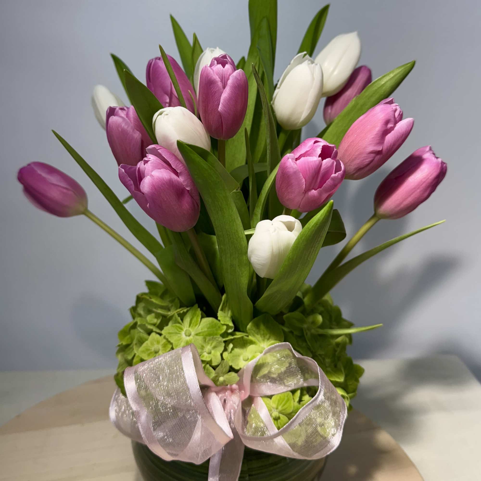 Pink and white tulips arranged in a round vase with a ribbon bow