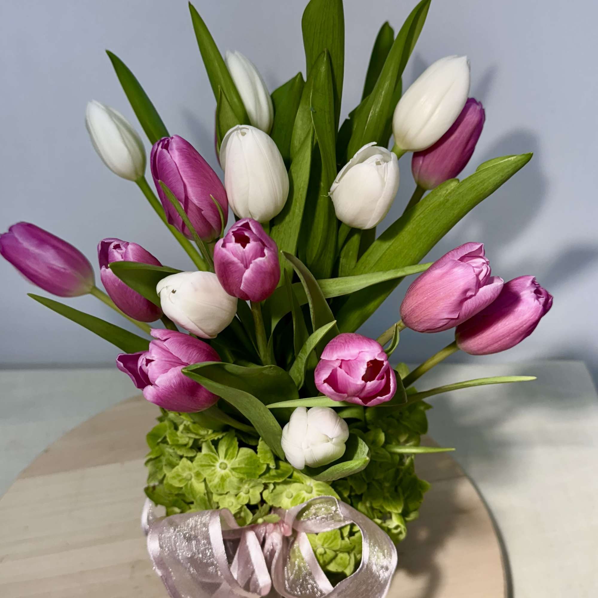 Pink and white tulips arranged in a vase with a ribbon bow