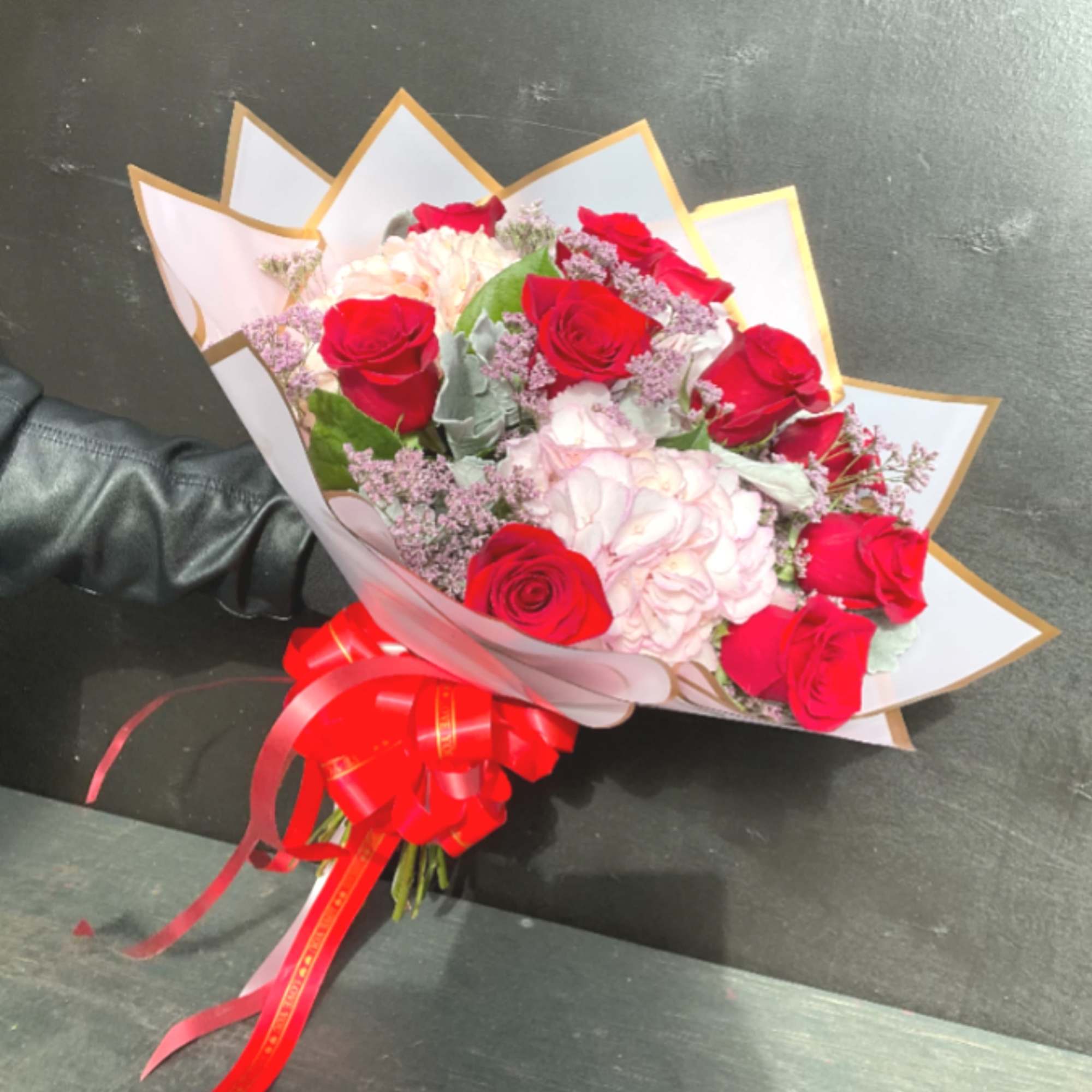 Bouquet of red roses and pale pink flowers wrapped in white paper with a red ribbon