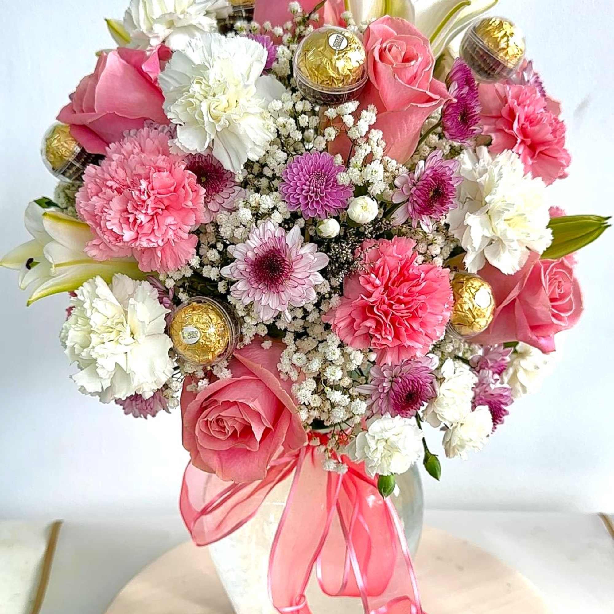 Pink and white bouquet in a glass vase with gold chocolates and a pink ribbon