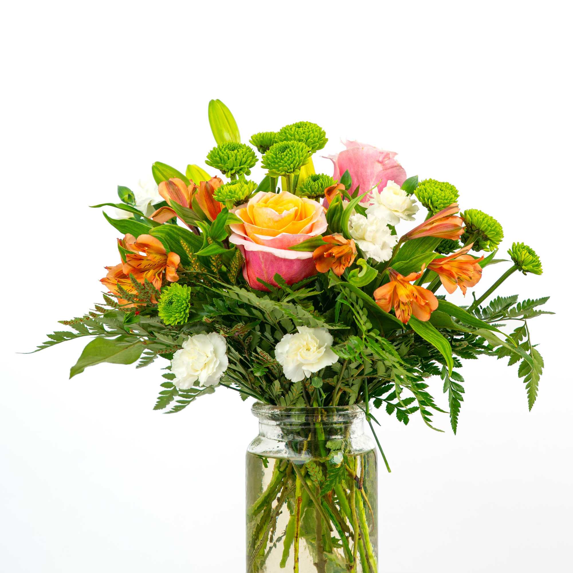 Bright mixed bouquet of roses, orange alstroemeria, green button mums, and white blooms in a clear glass jar.