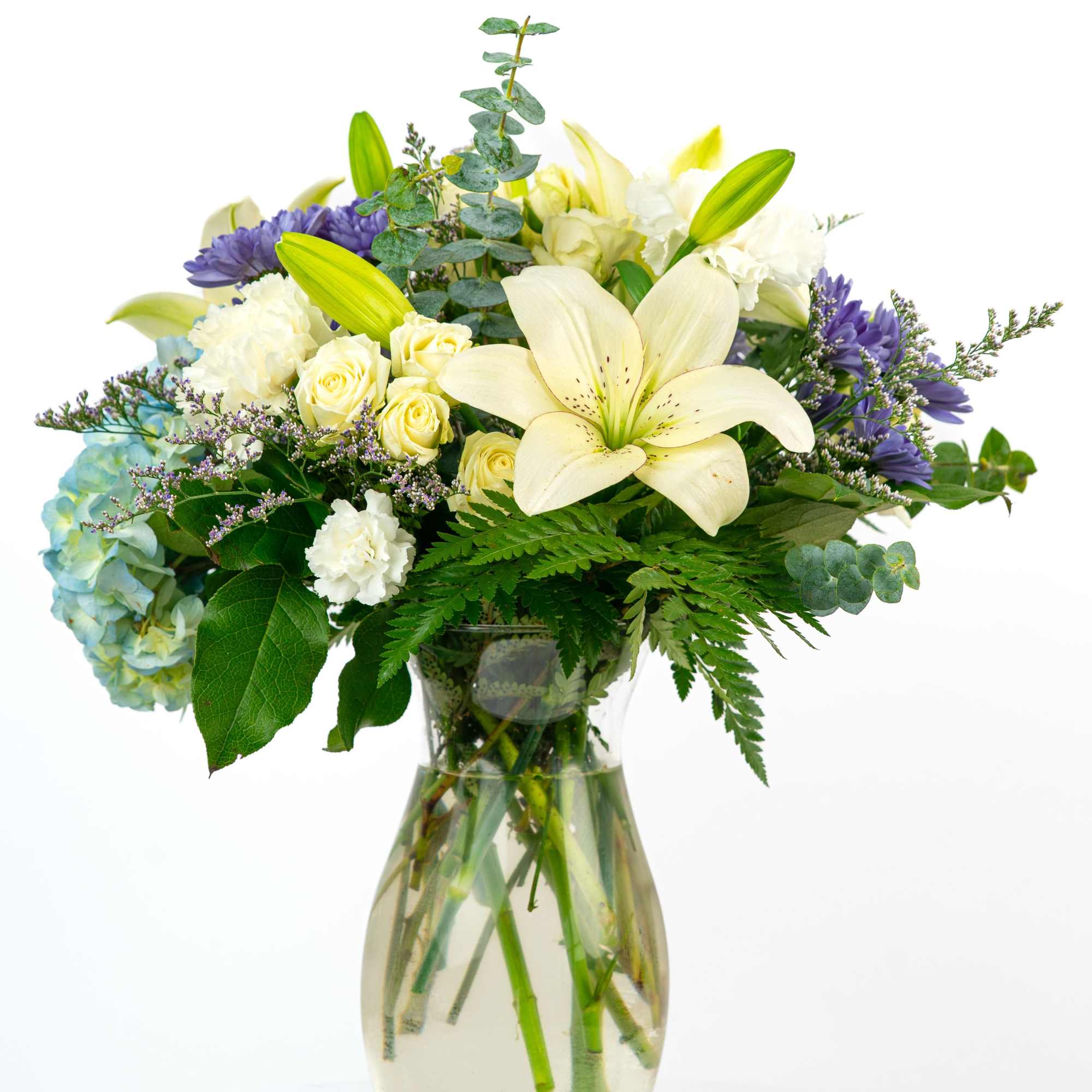 White lilies and roses in a glass vase with blue hydrangea and purple flowers