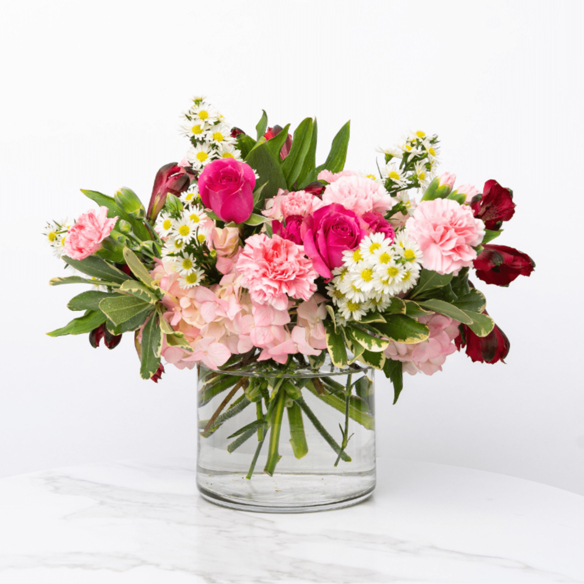 Pink roses, carnations, hydrangea, and white daisies in a clear glass vase