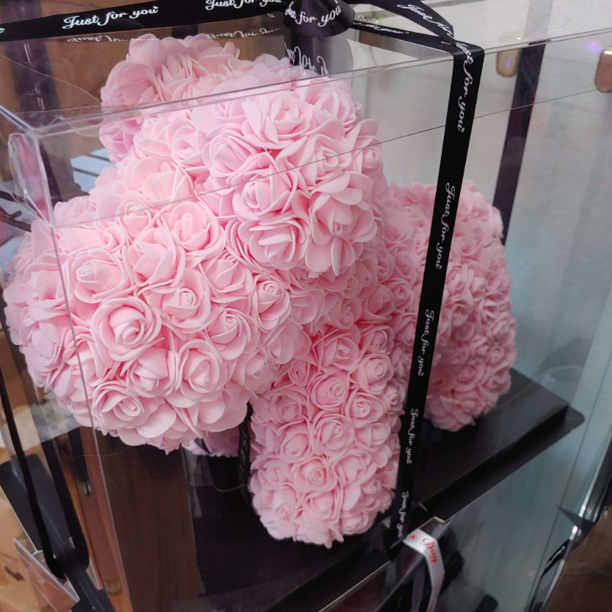 Pink rose-shaped floral arrangement in a clear box with a black ribbon