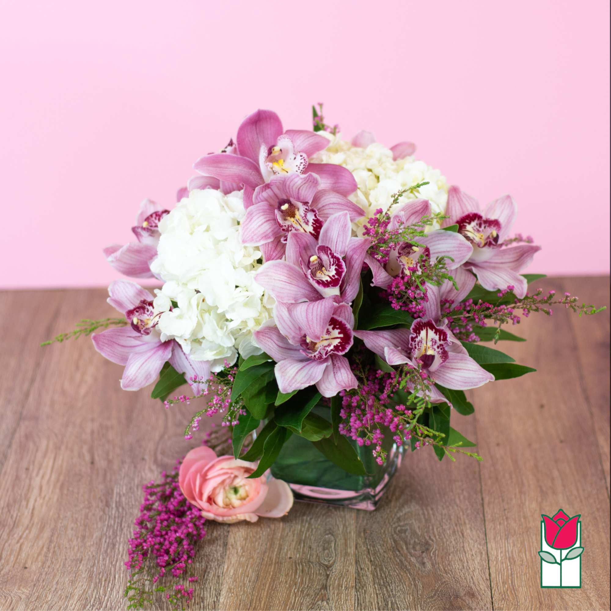 Pink orchids and white hydrangeas in a glass vase with a pink bloom on the table