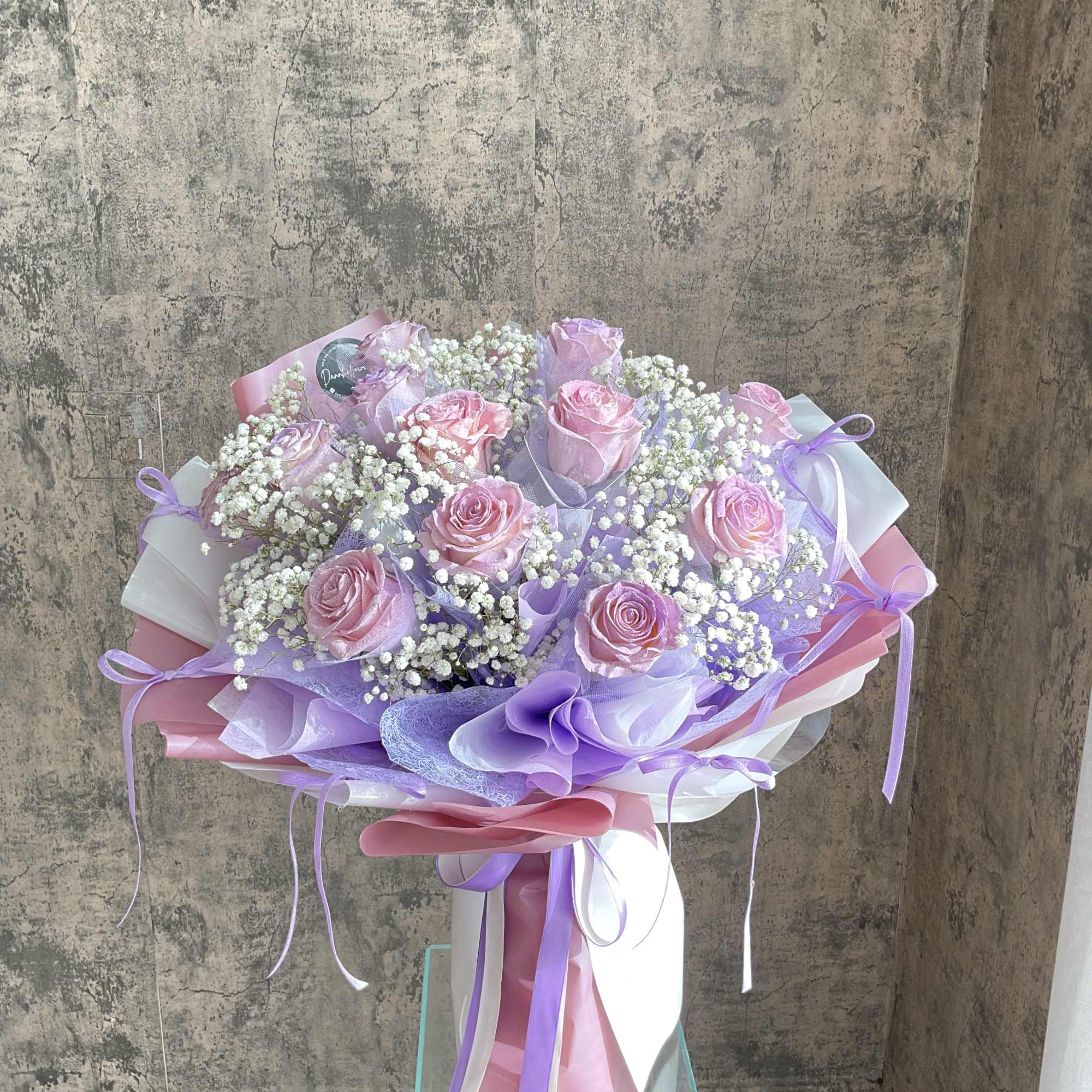 Bouquet of pink roses and baby's breath wrapped in lavender and white paper