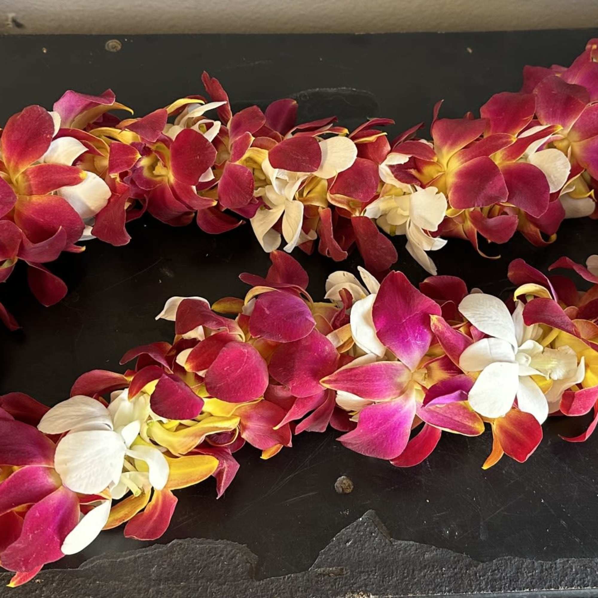 Two orchid leis in pink, white, and yellow on a dark surface
