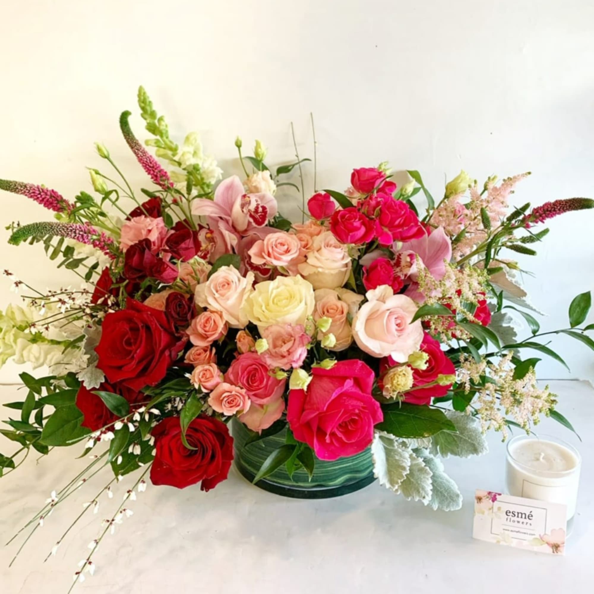 Mixed bouquet of red, pink, and cream roses with orchids in a green vase