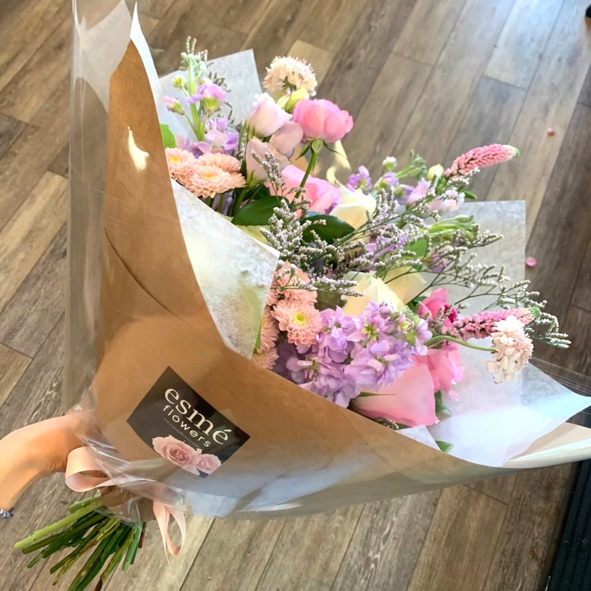 Handheld bouquet of pink and lavender flowers wrapped in paper