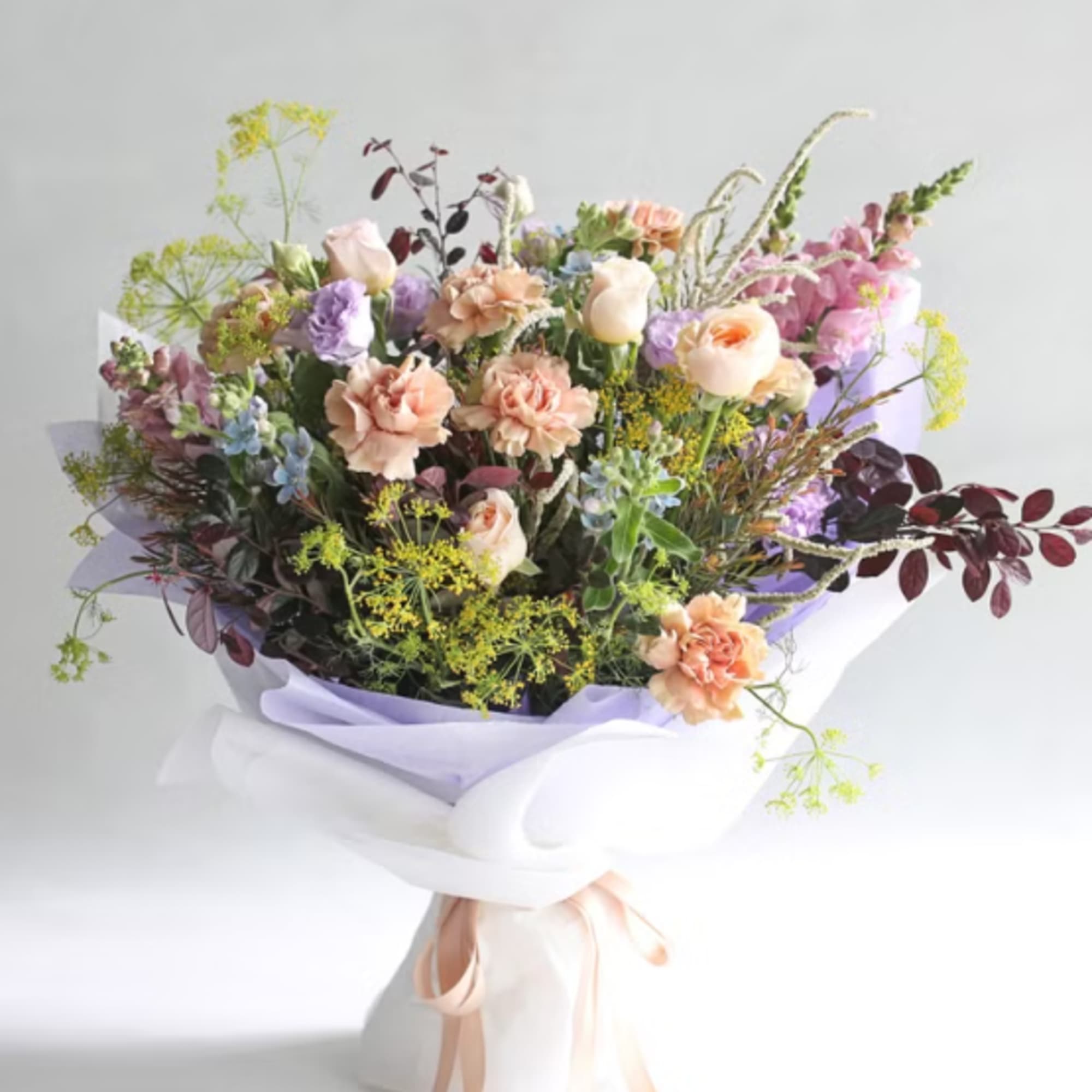 Pastel bouquet of mixed flowers wrapped in white and lavender paper