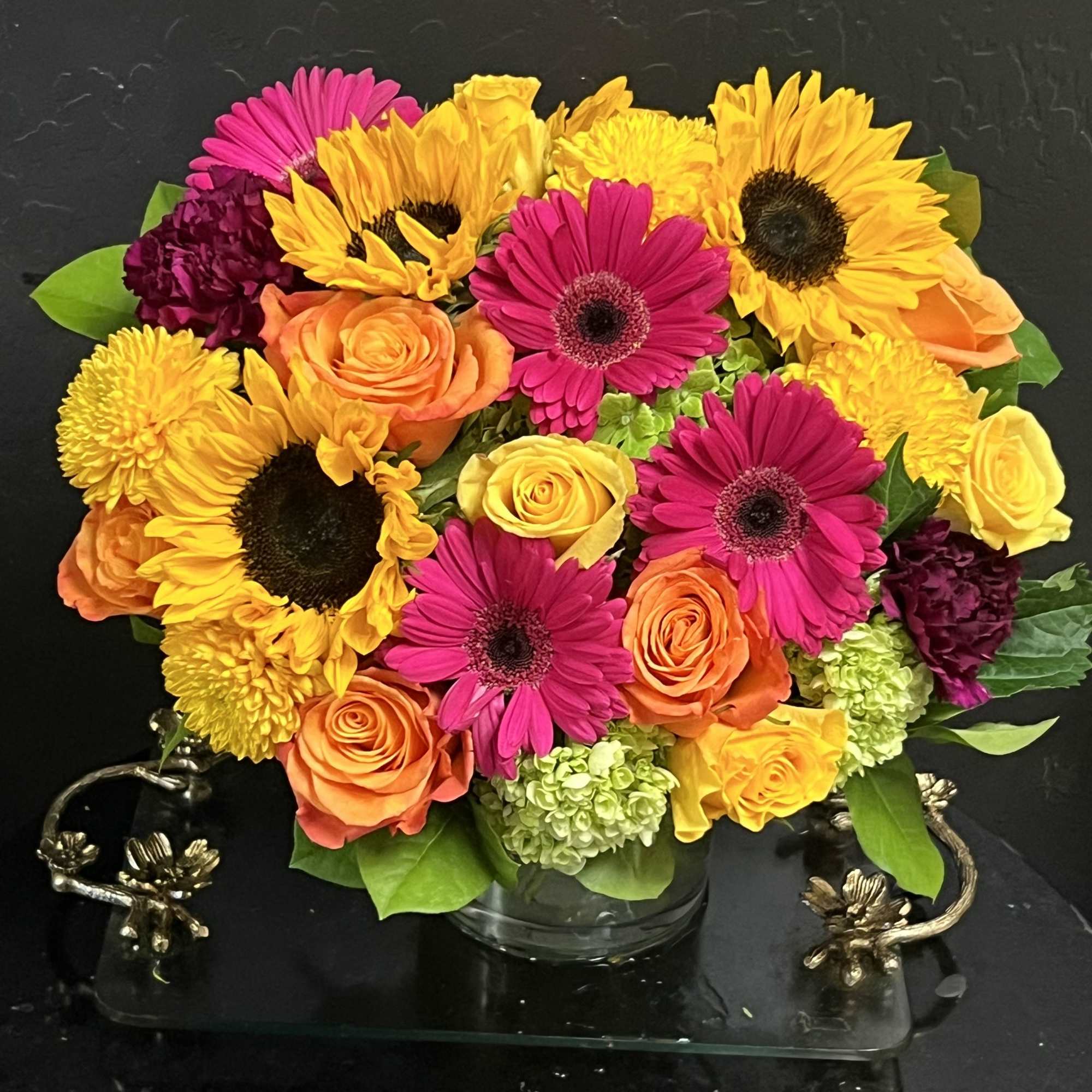 Bright mixed bouquet of sunflowers, gerbera daisies, and roses in a glass vase