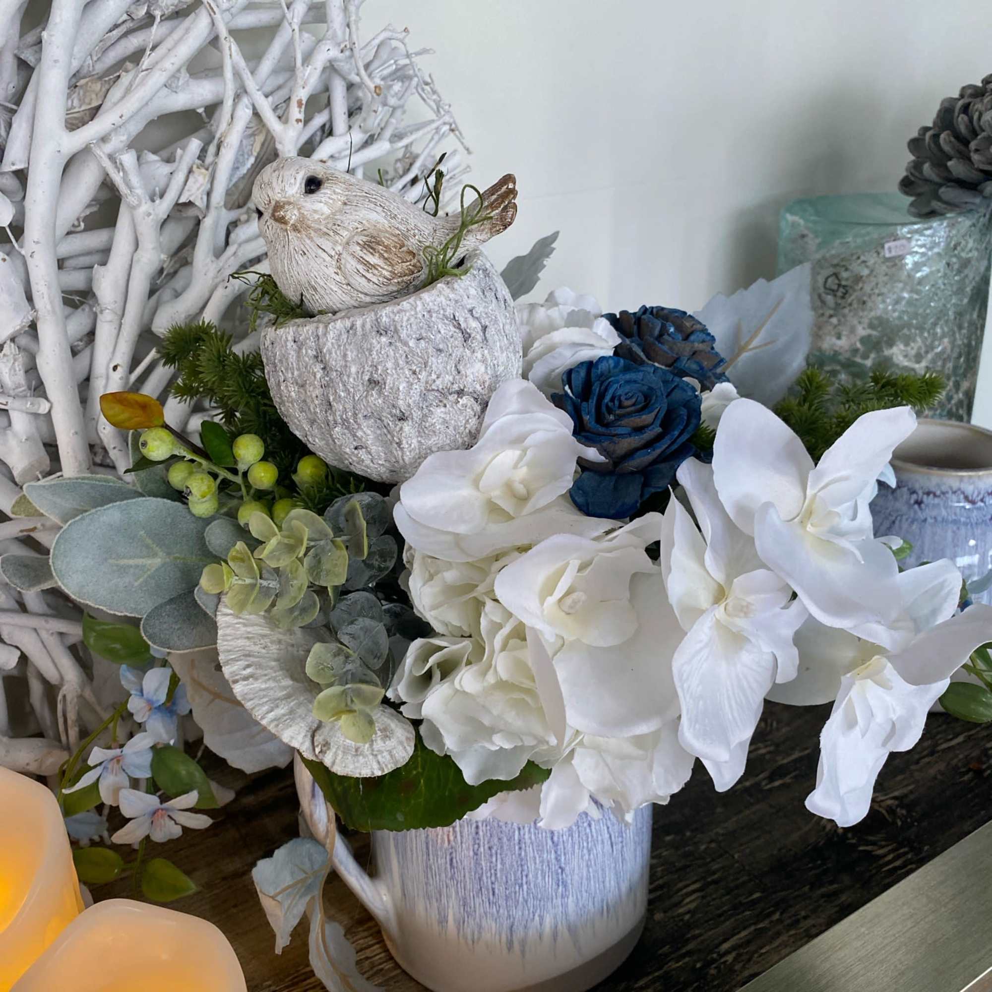White and blue floral arrangement in a ceramic pot with a bird figurine
