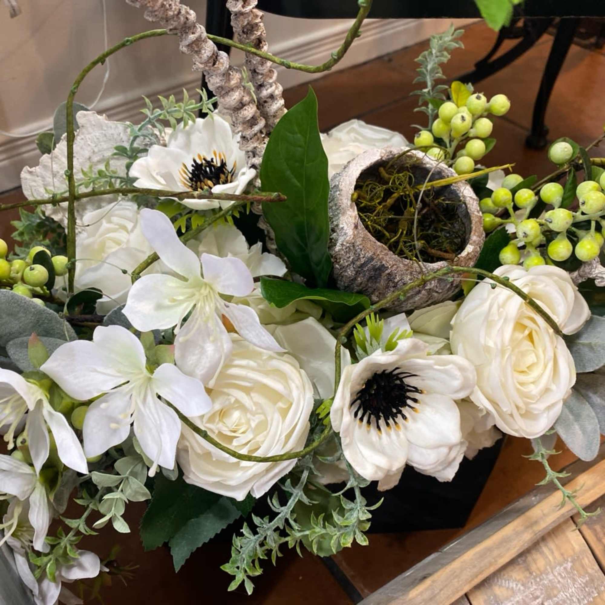 White floral arrangement with roses and anemones in a rustic container