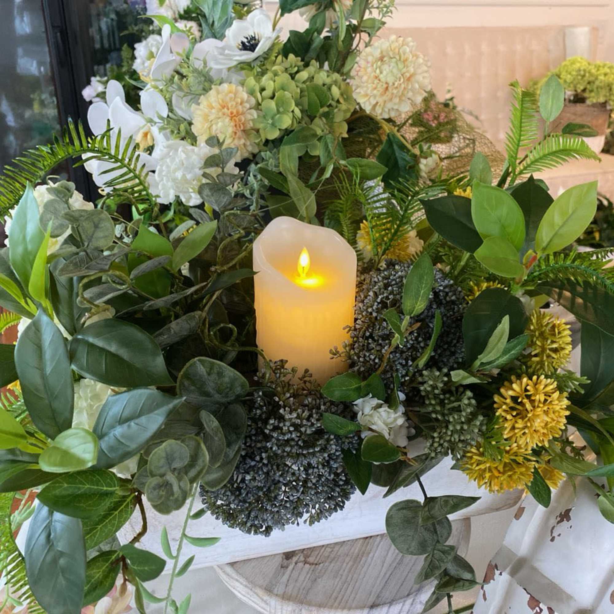 Floral centerpiece with white blooms and a lit candle in a white container