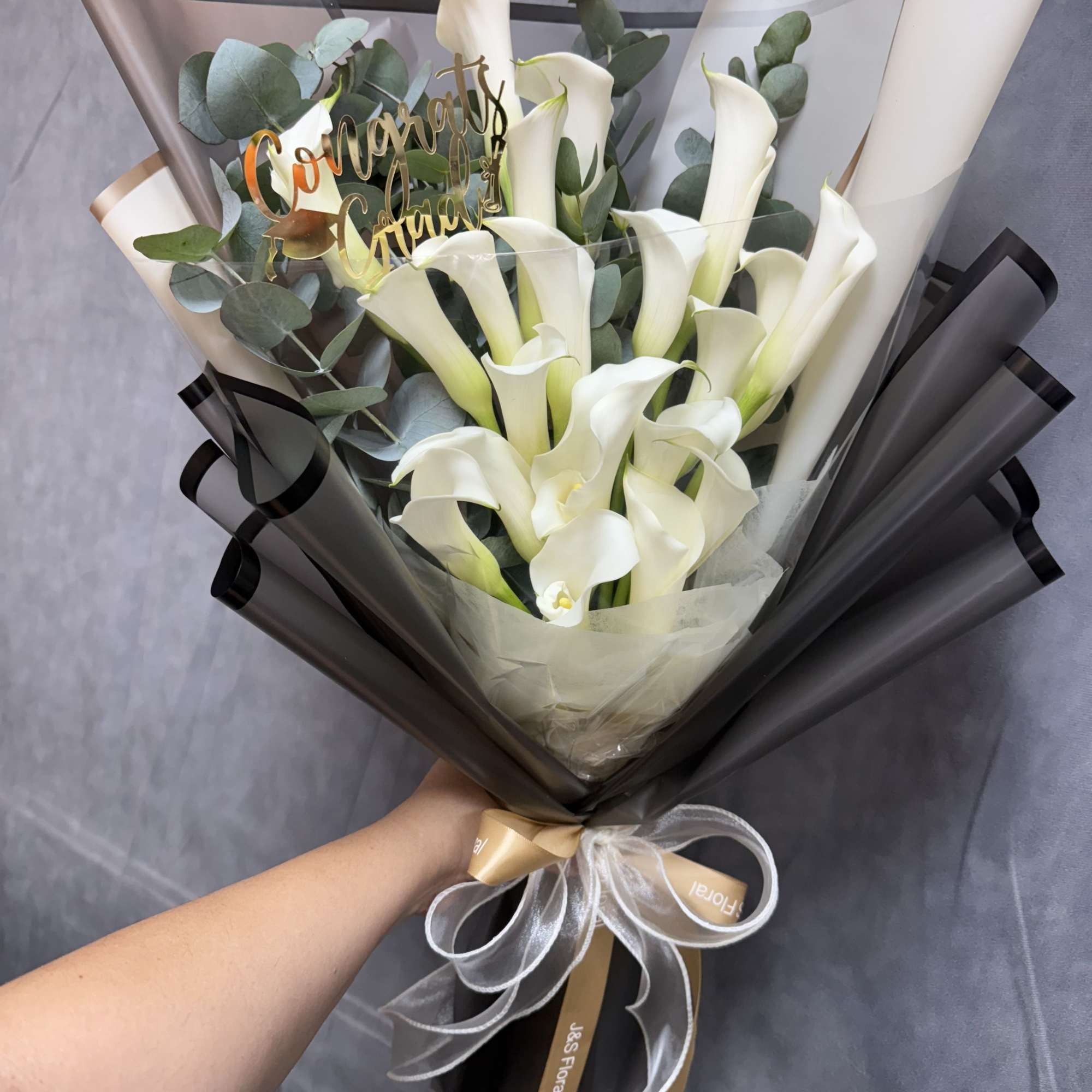 White calla lilies with eucalyptus, wrapped in black and translucent paper with
