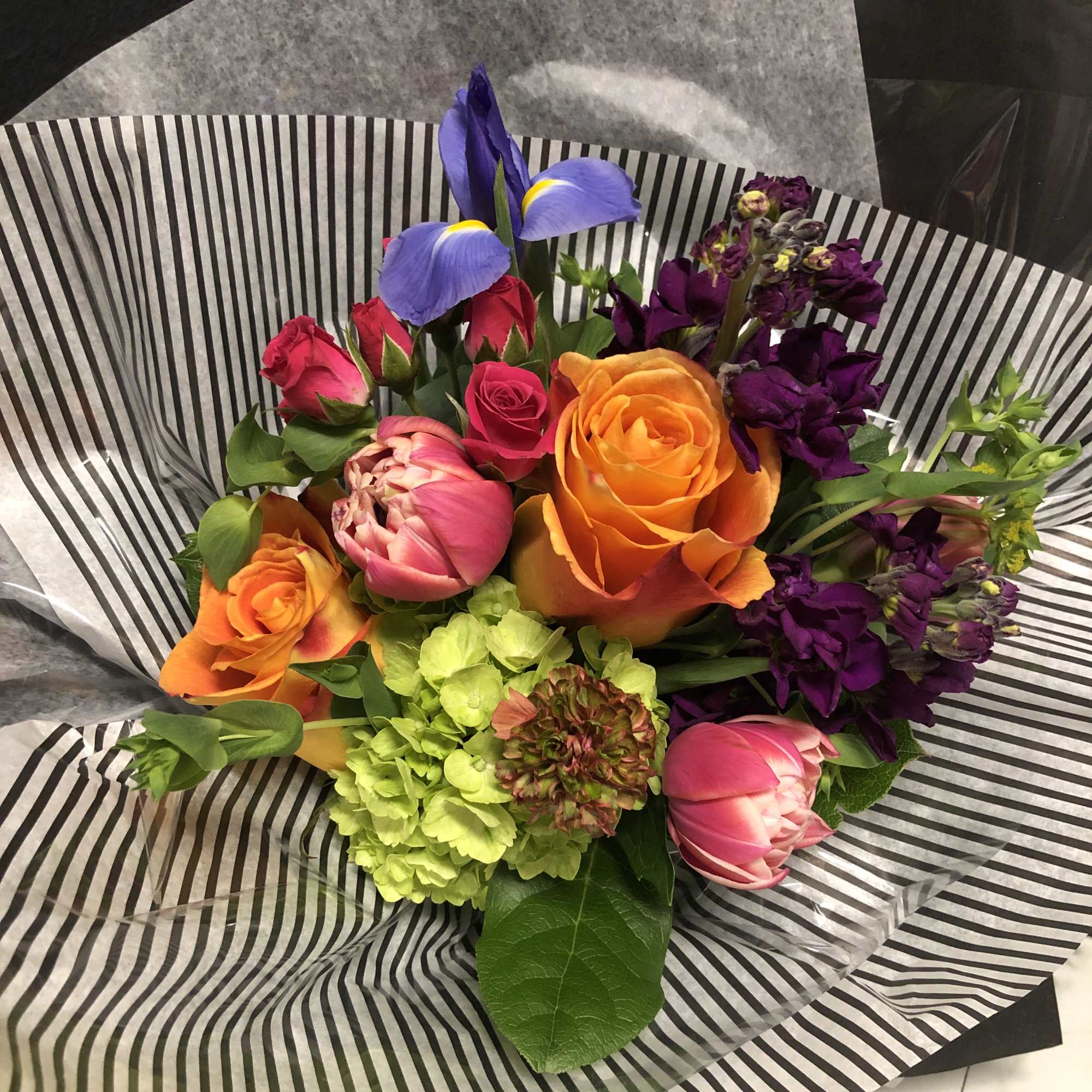 Colorful bouquet with roses, tulips, irises, and purple blooms wrapped in striped paper