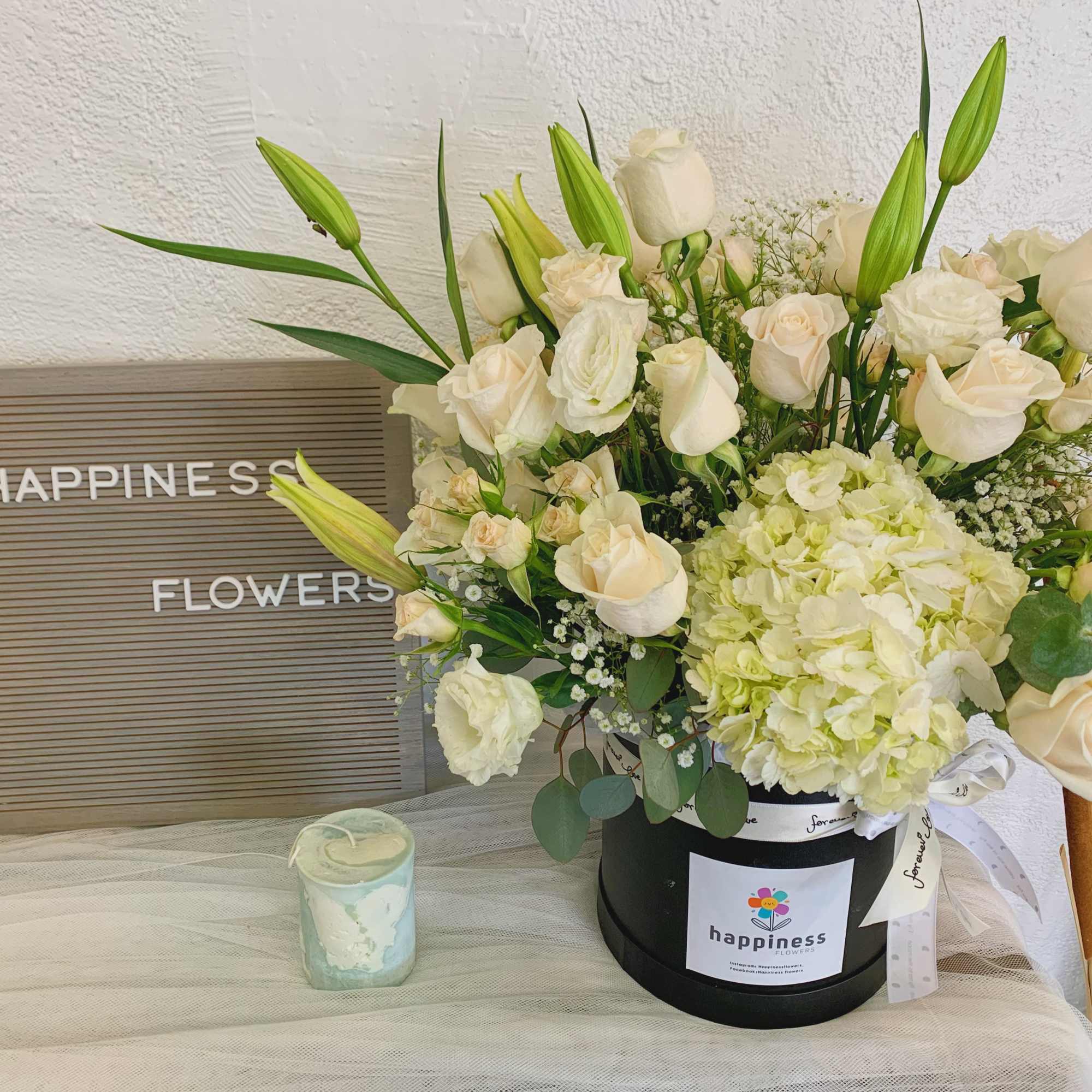 Cream roses and lilies arranged in a black hatbox with a ribbon.
