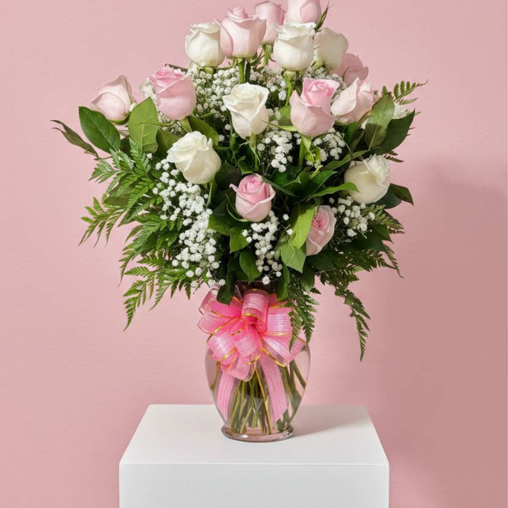 Pink and white roses in a glass vase with a pink ribbon