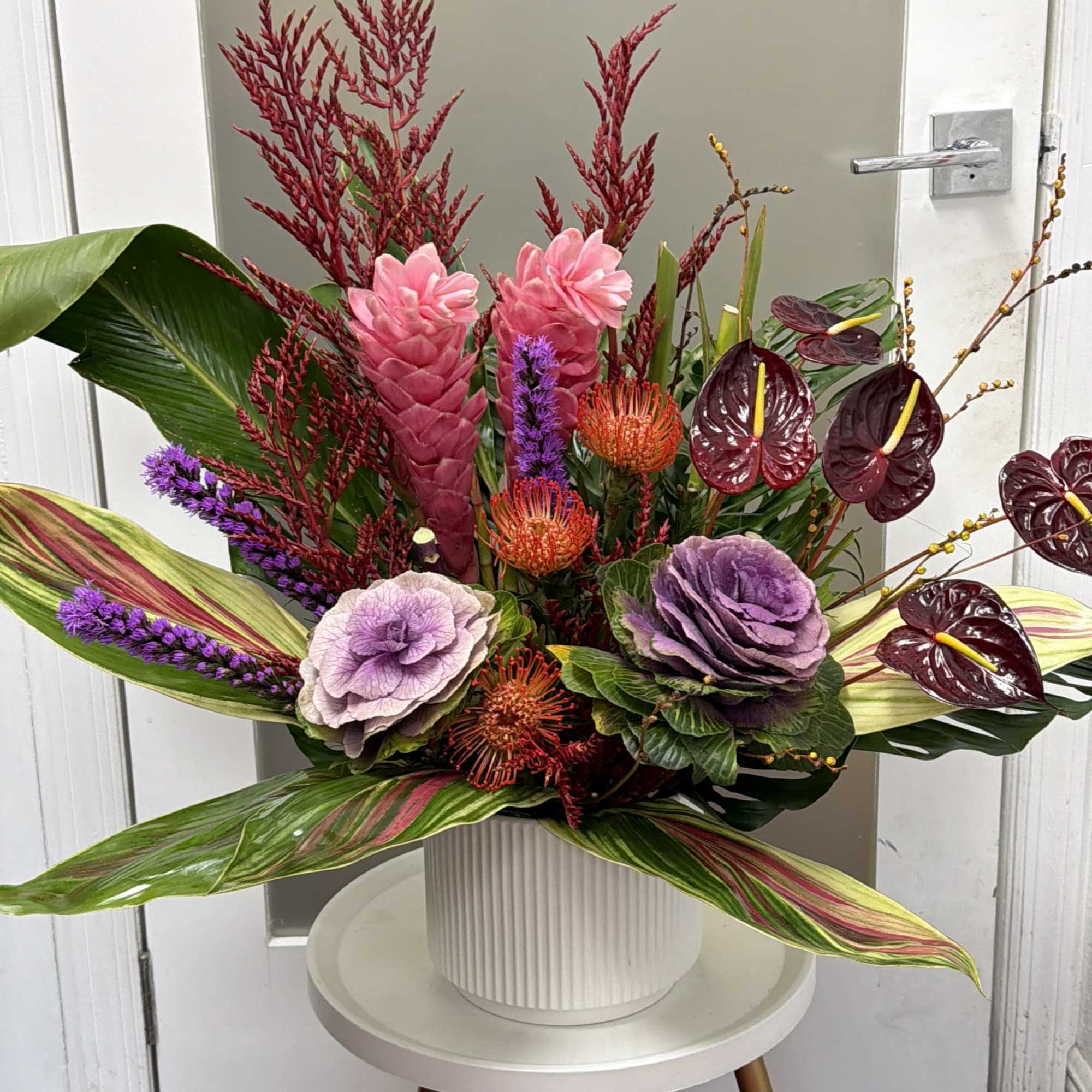 Tropical floral arrangement in a white vase with pink, purple, and burgundy blooms