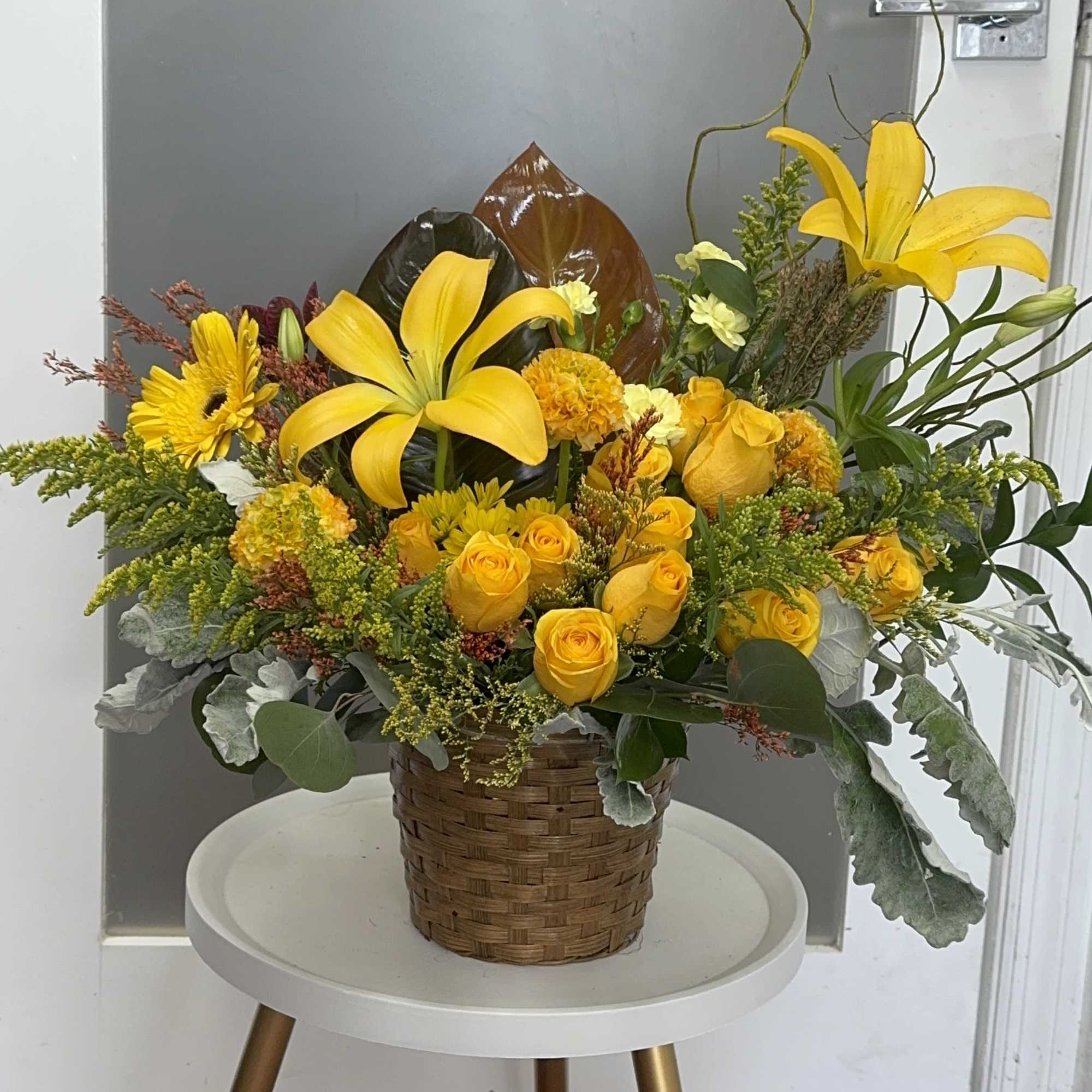 Yellow floral arrangement in a woven basket with lilies and roses