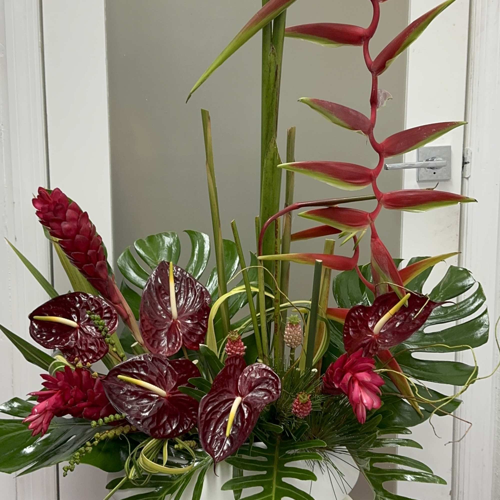Tropical arrangement with red heliconia and burgundy anthuriums in a white container