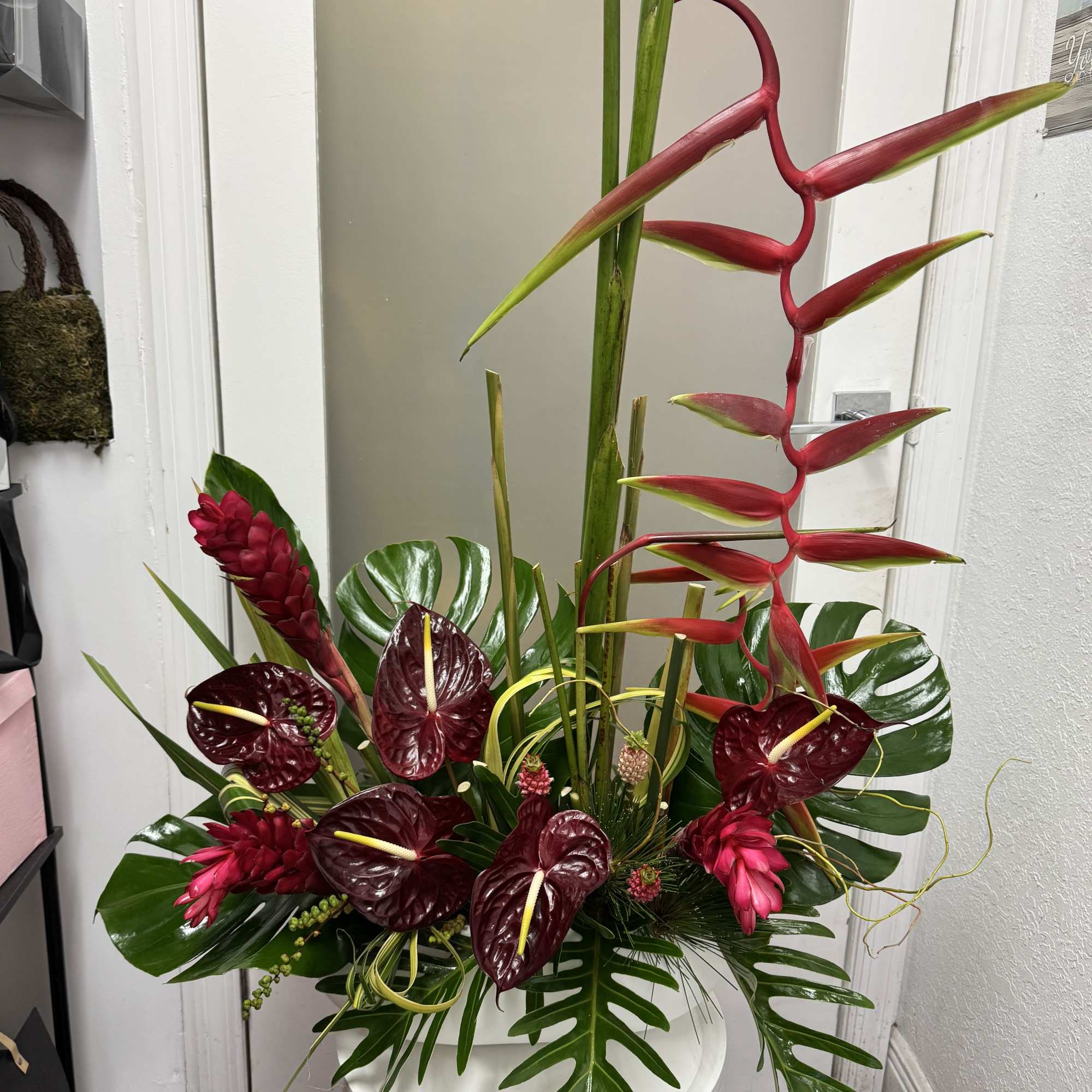 Tropical floral arrangement with red heliconia and burgundy anthuriums in a white vase