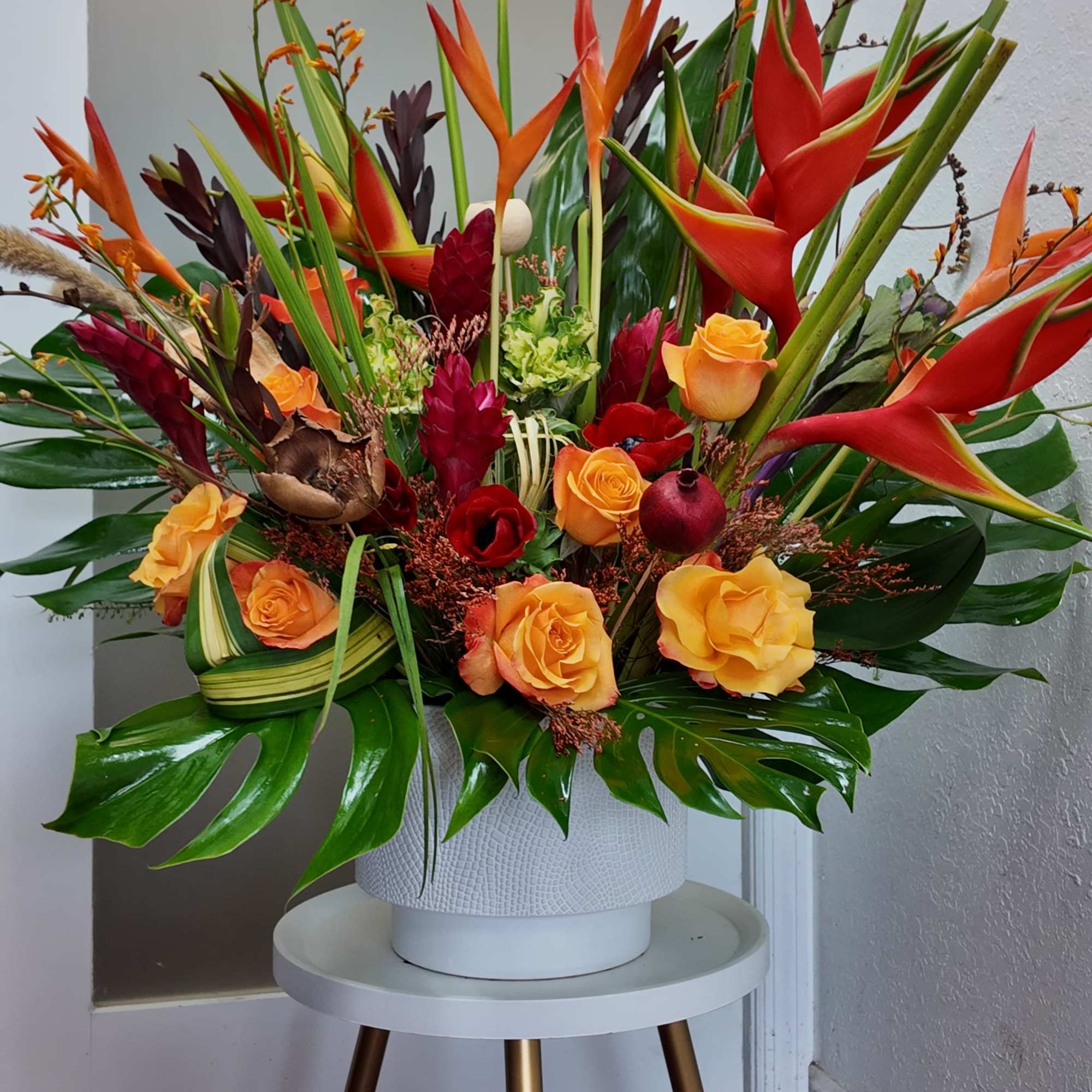 Large tropical arrangement with orange heliconia and yellow roses in a white vase