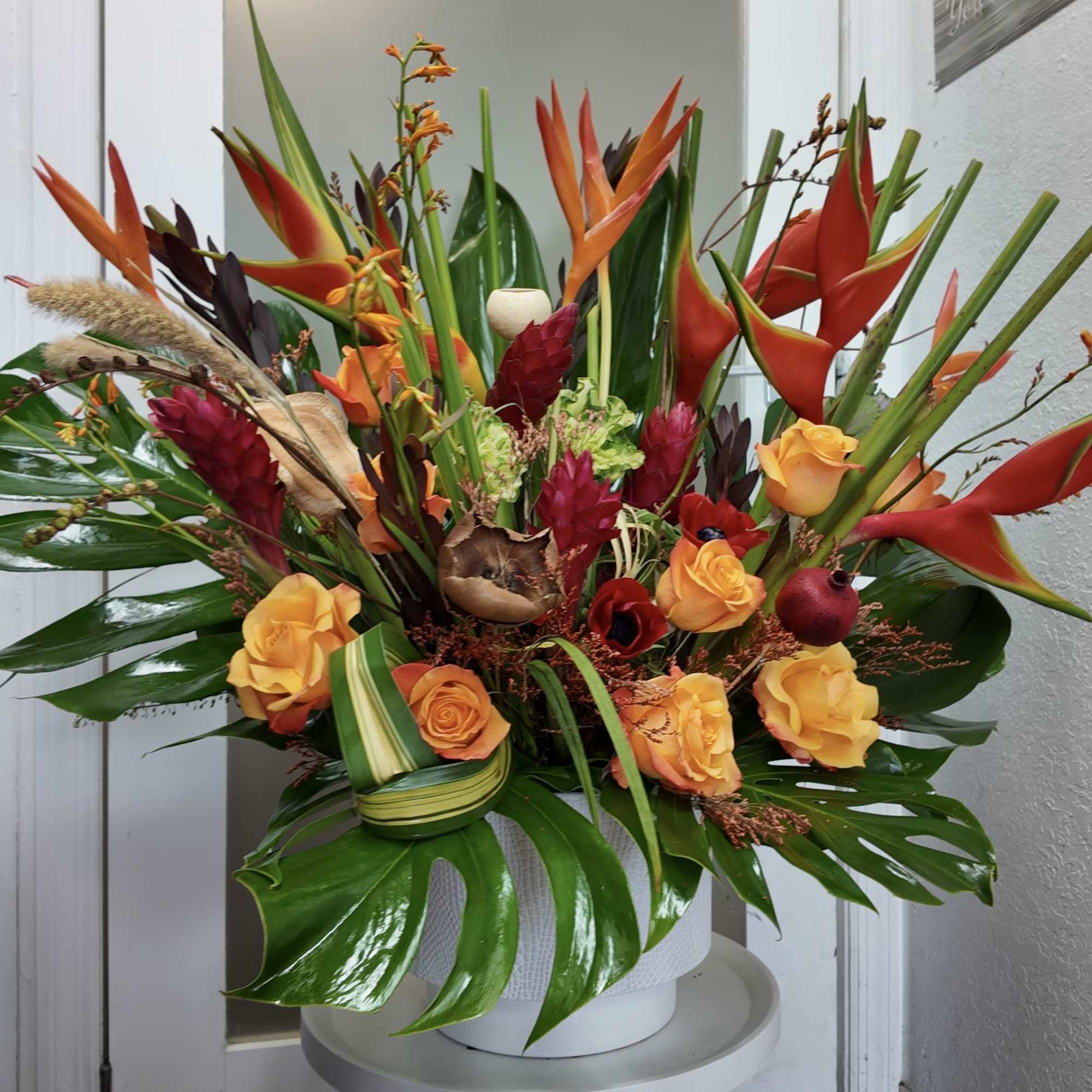 Tropical arrangement with orange heliconia and yellow roses in a white vase