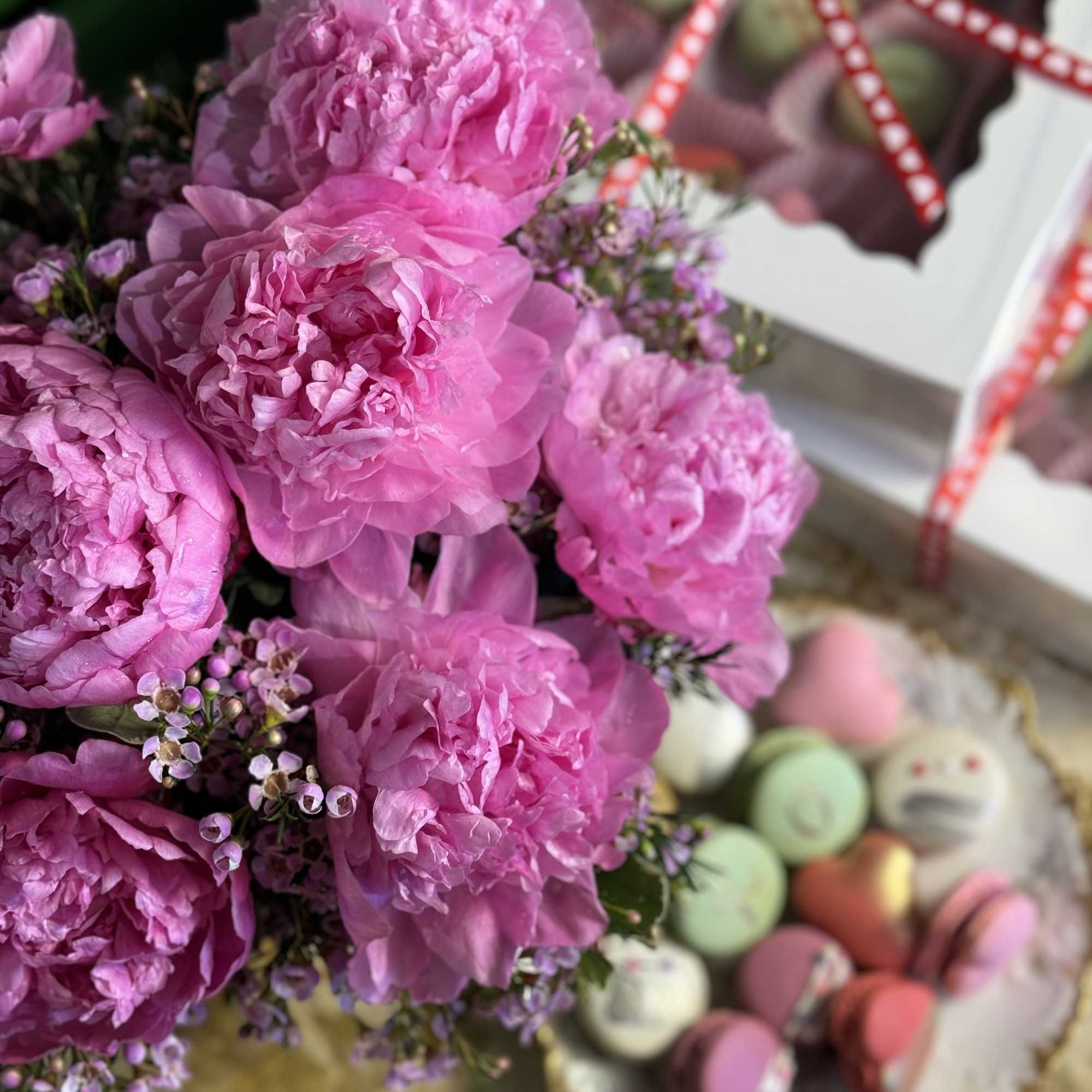 Pink peonies with small purple filler flowers beside a tray of macarons