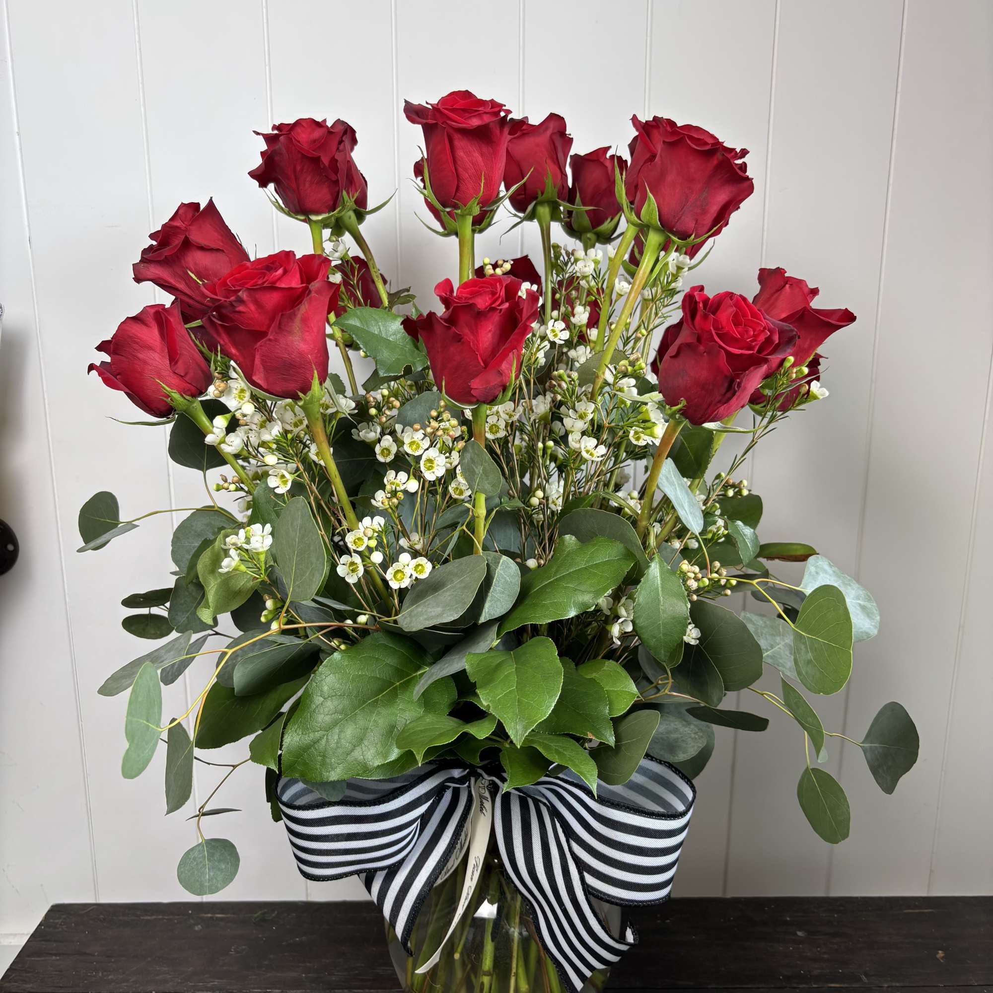 Red roses arranged in a clear glass vase with a striped ribbon.