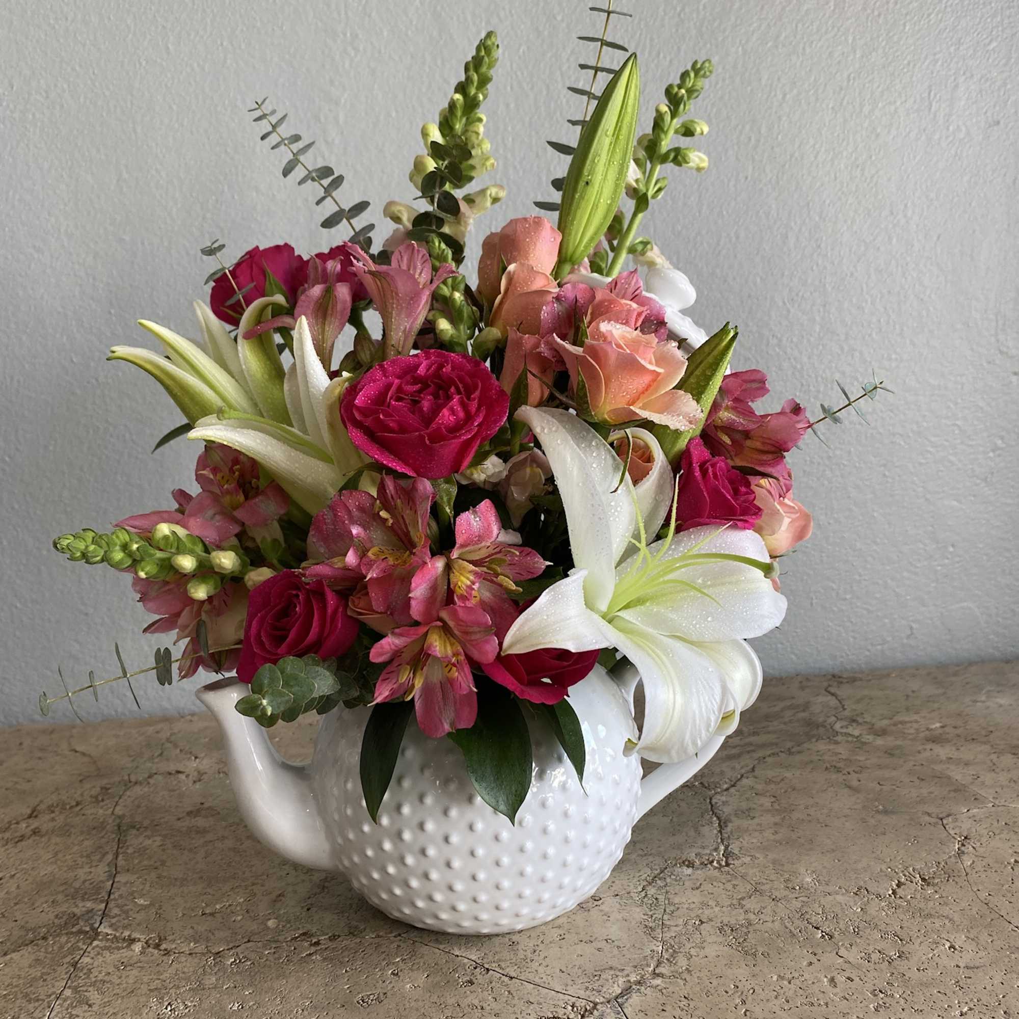 Pink and white mixed flower arrangement in a white teapot vase