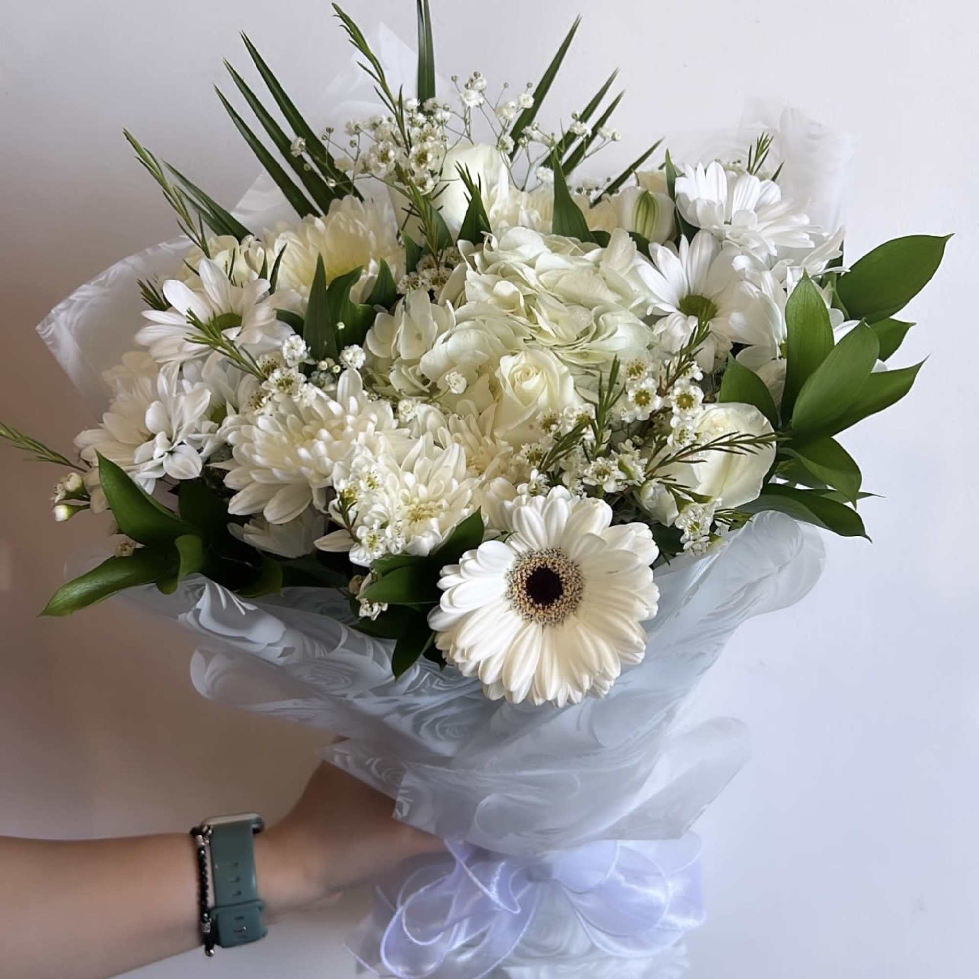 White bouquet with daisies, roses, and greenery wrapped in sheer paper