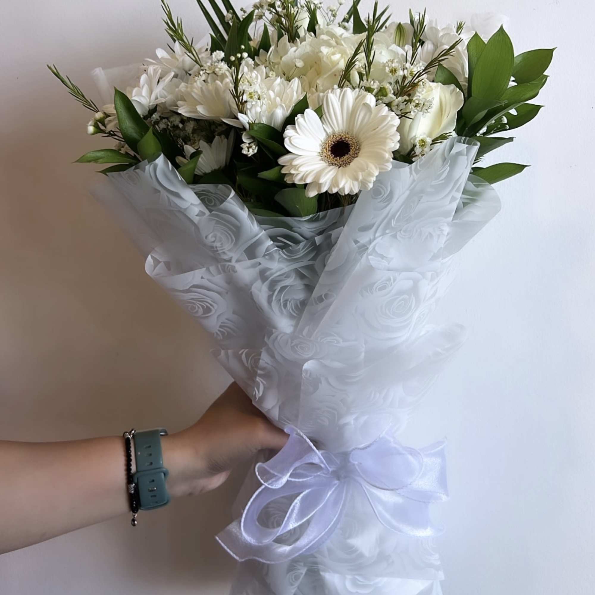 White bouquet with gerbera daisies and roses wrapped in sheer ribboned paper