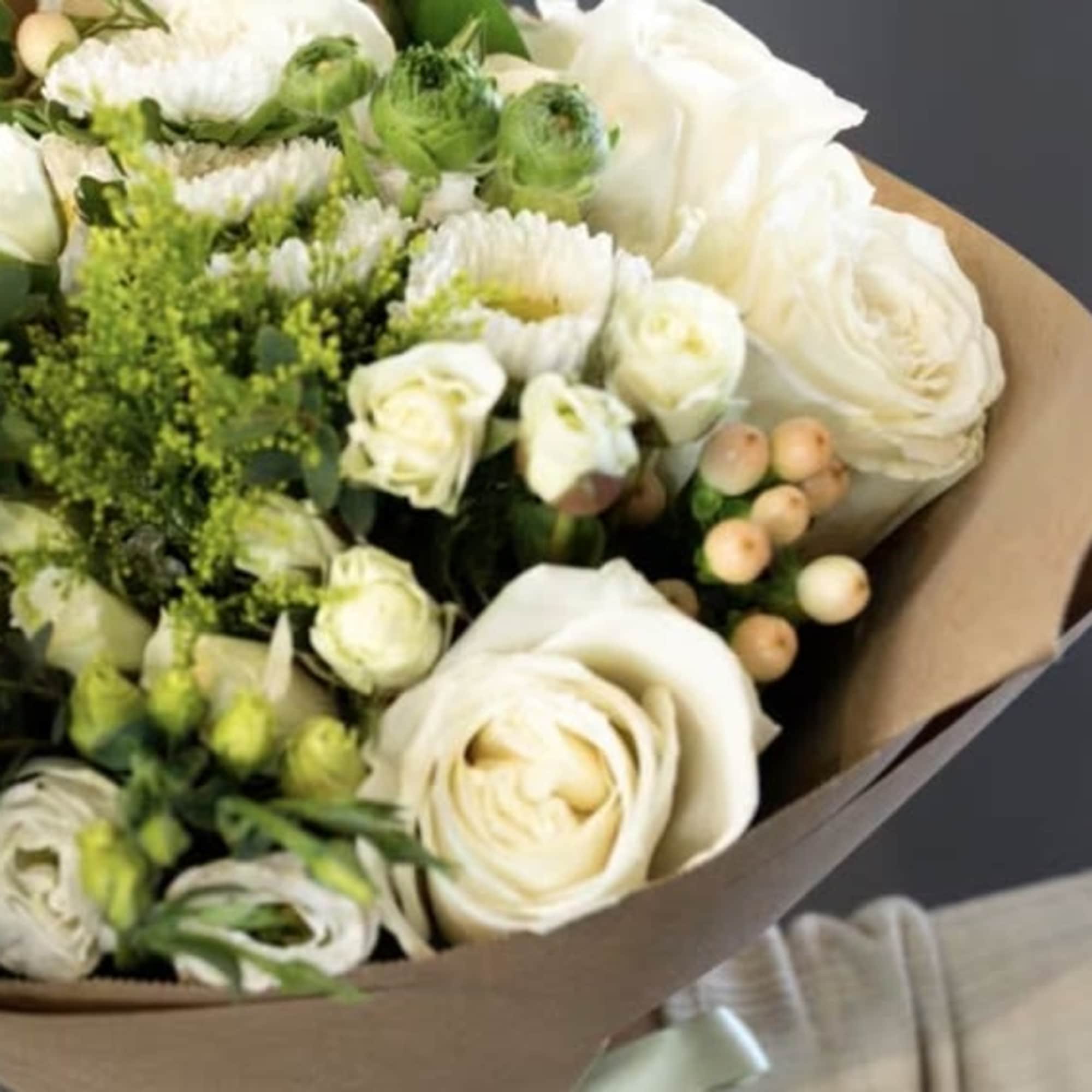 Bouquet of white roses and green filler flowers wrapped in brown paper