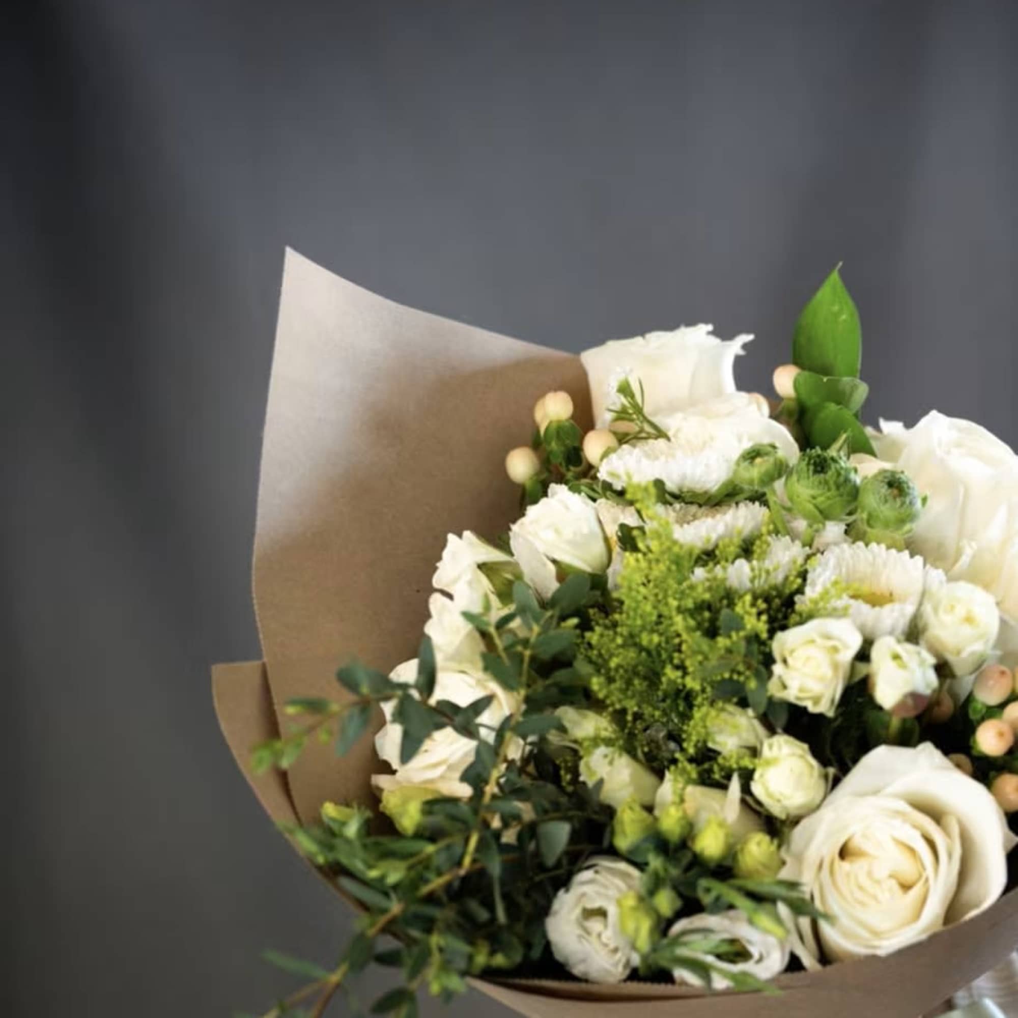 Bouquet of white roses and green flowers wrapped in brown paper