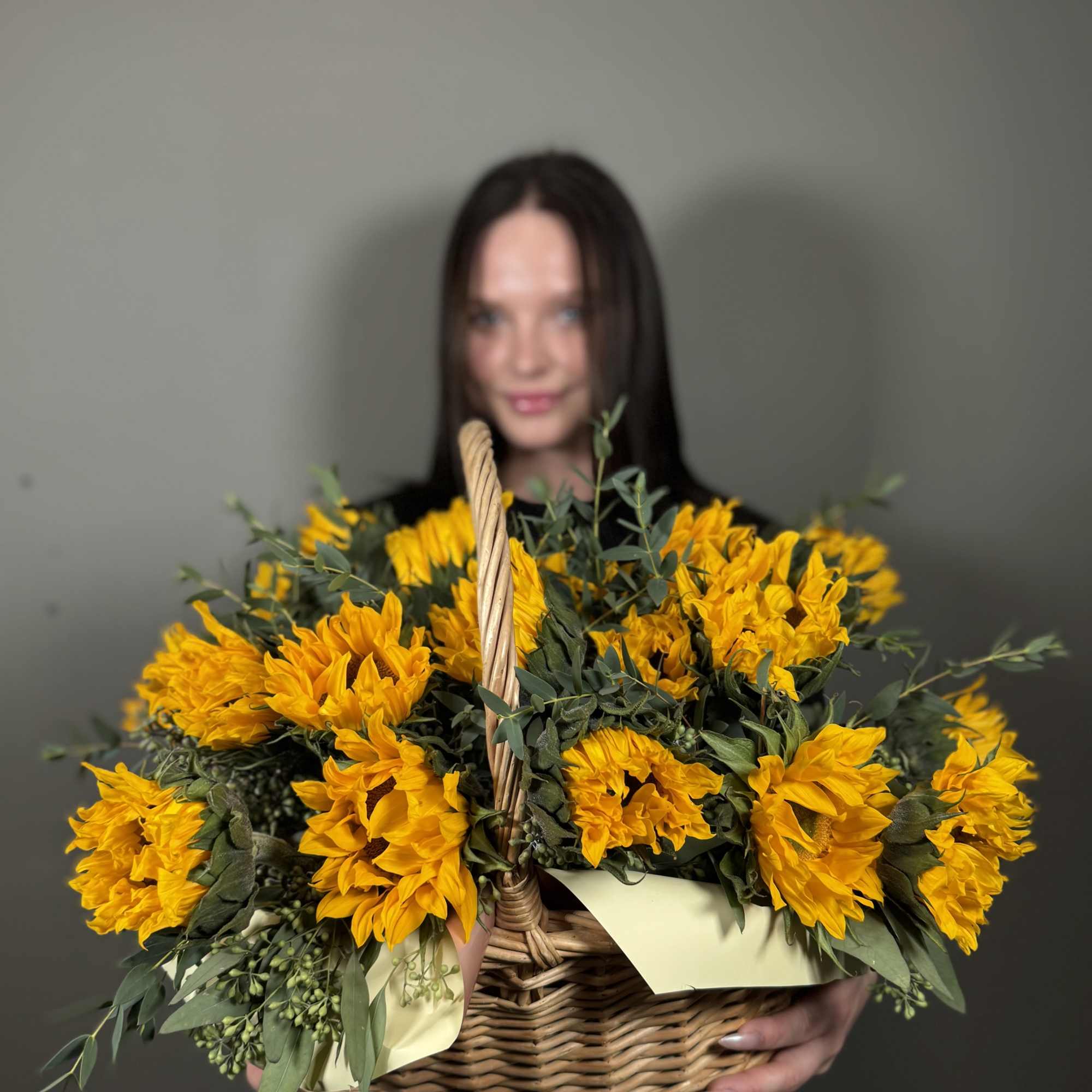 Basket of yellow flowers with greenery held by a person